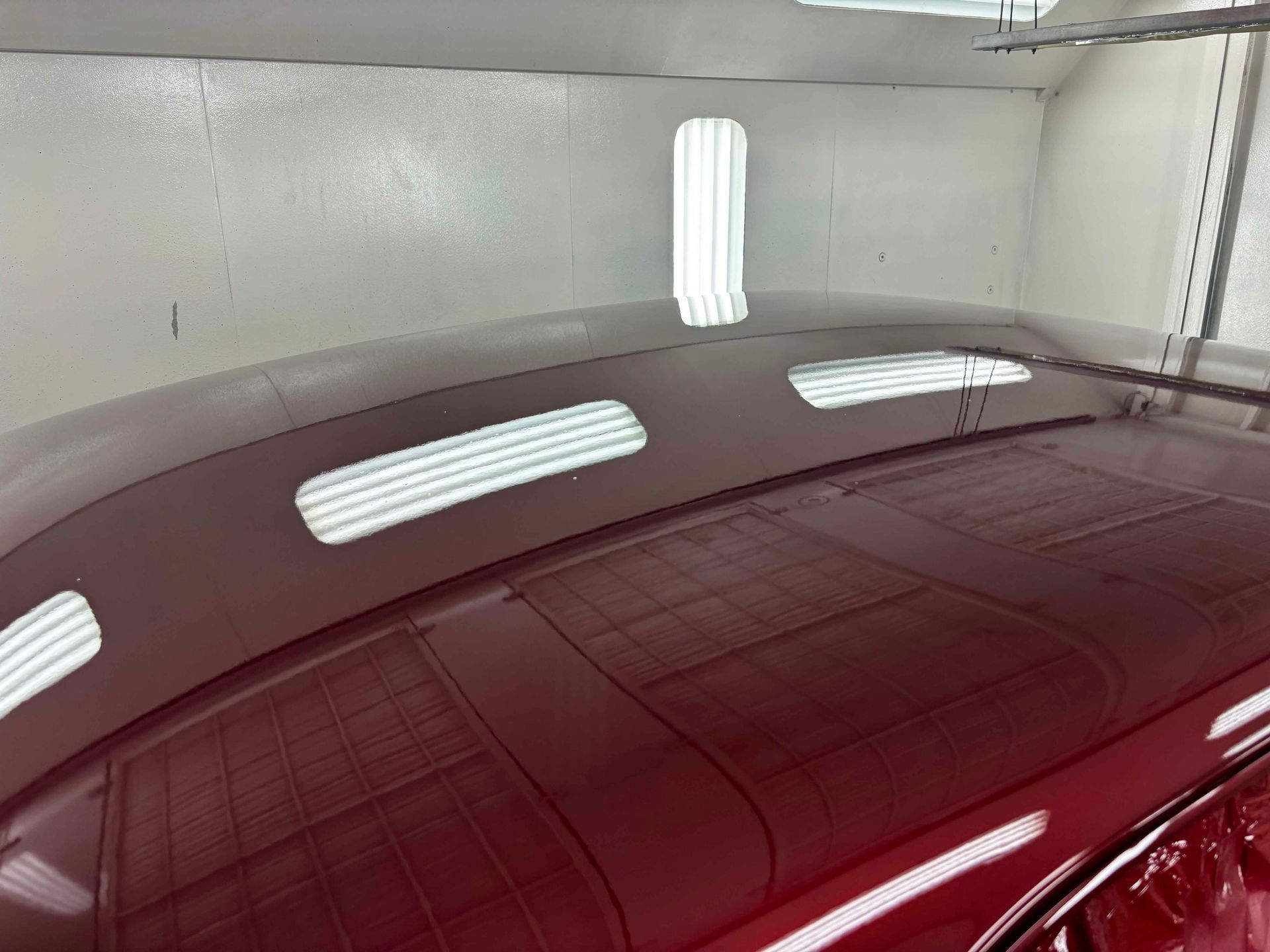 Glossy maroon car roof in a garage, reflecting bright overhead lights