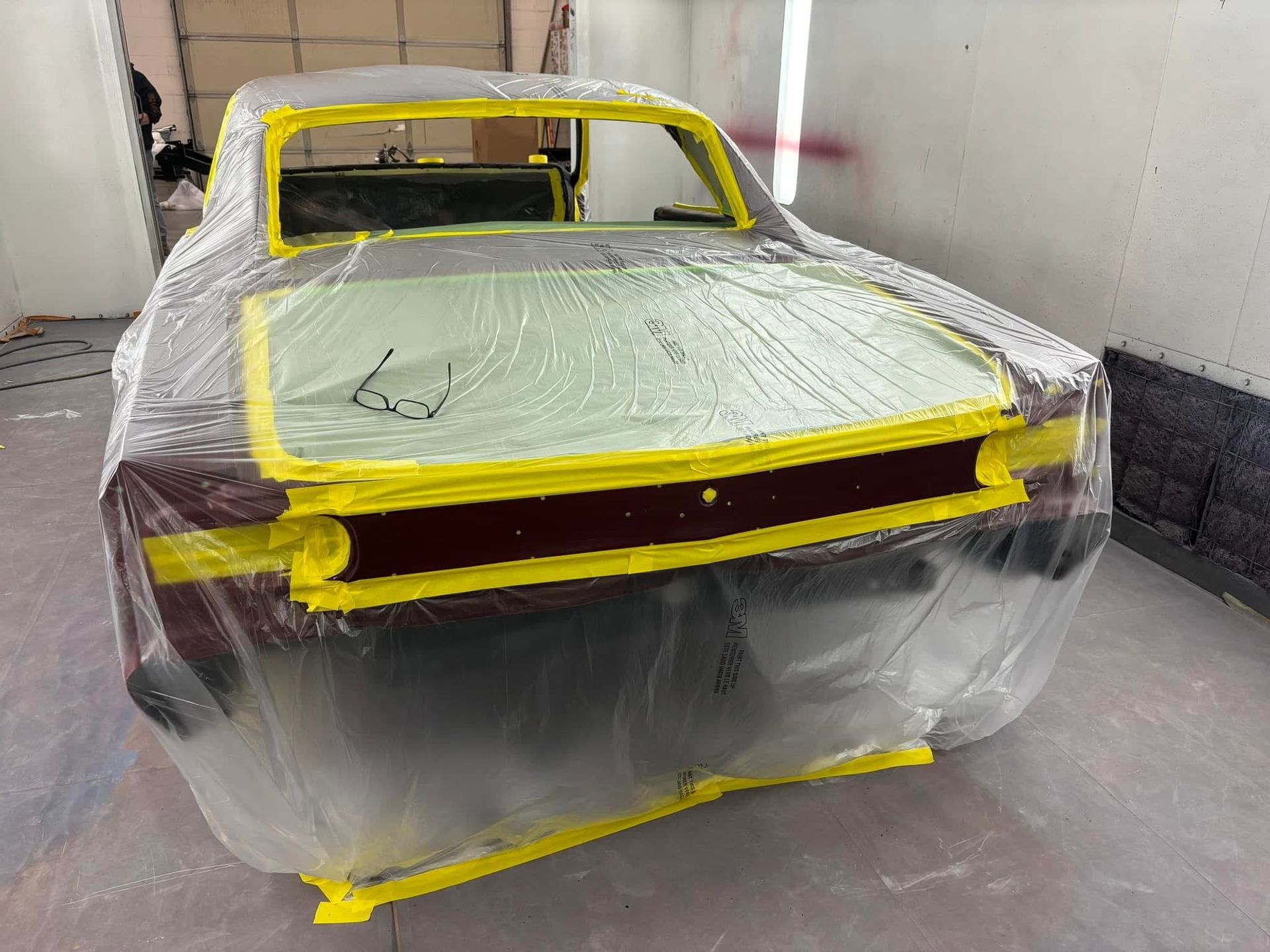 Car body in a workshop, wrapped in plastic and masked with yellow tape for painting
