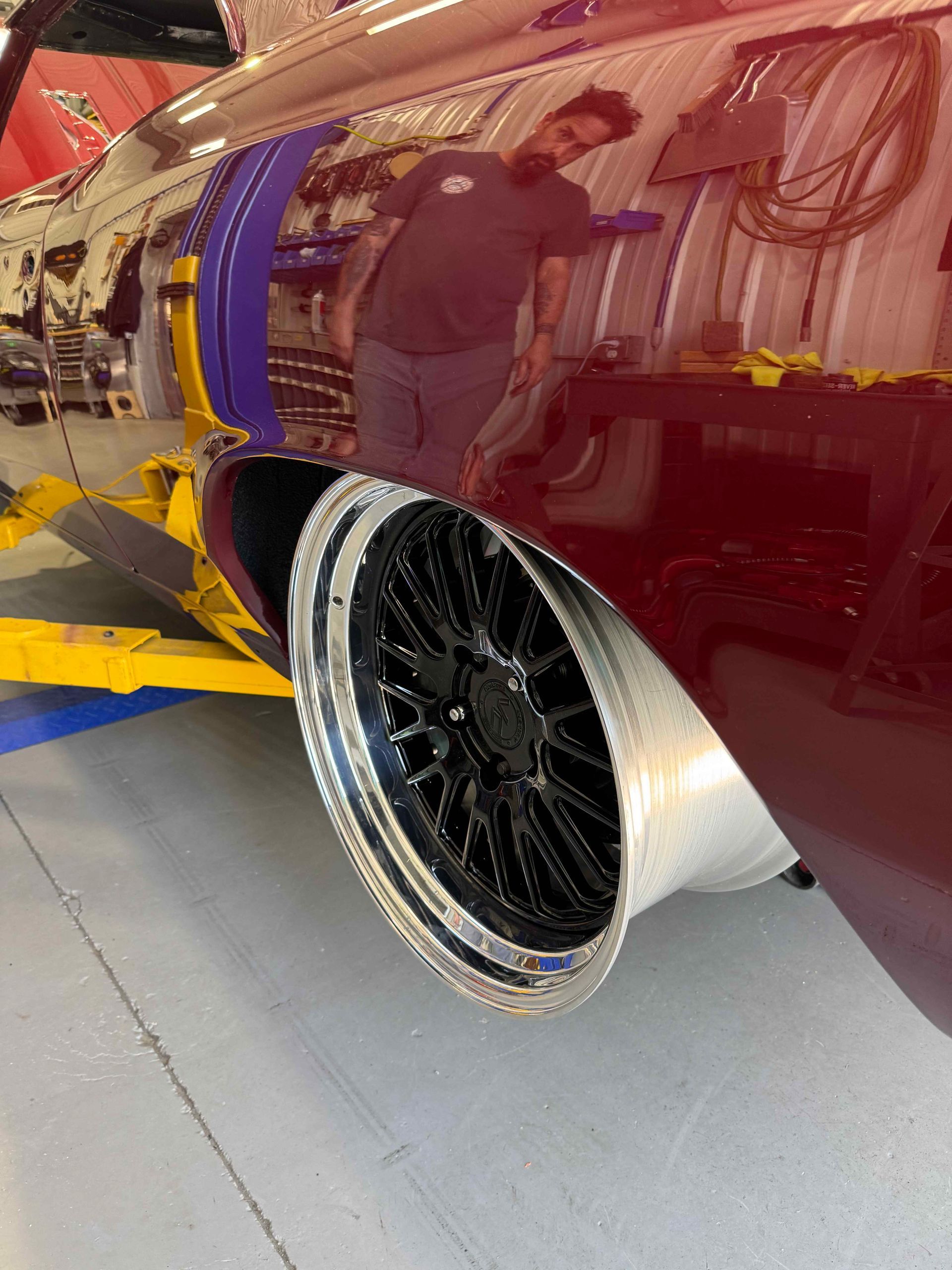 Maroon car with black custom wheel and chrome lip in a garage, with a person reflected in the paint