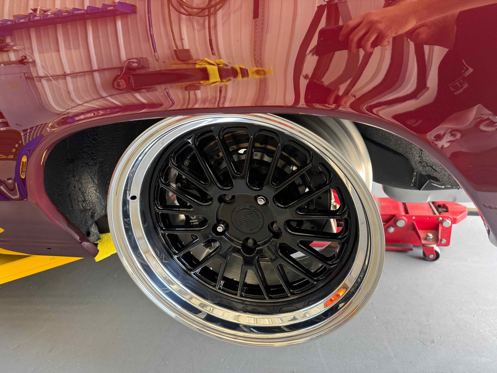 Shiny black custom wheel on a maroon car, viewed close-up in a garage