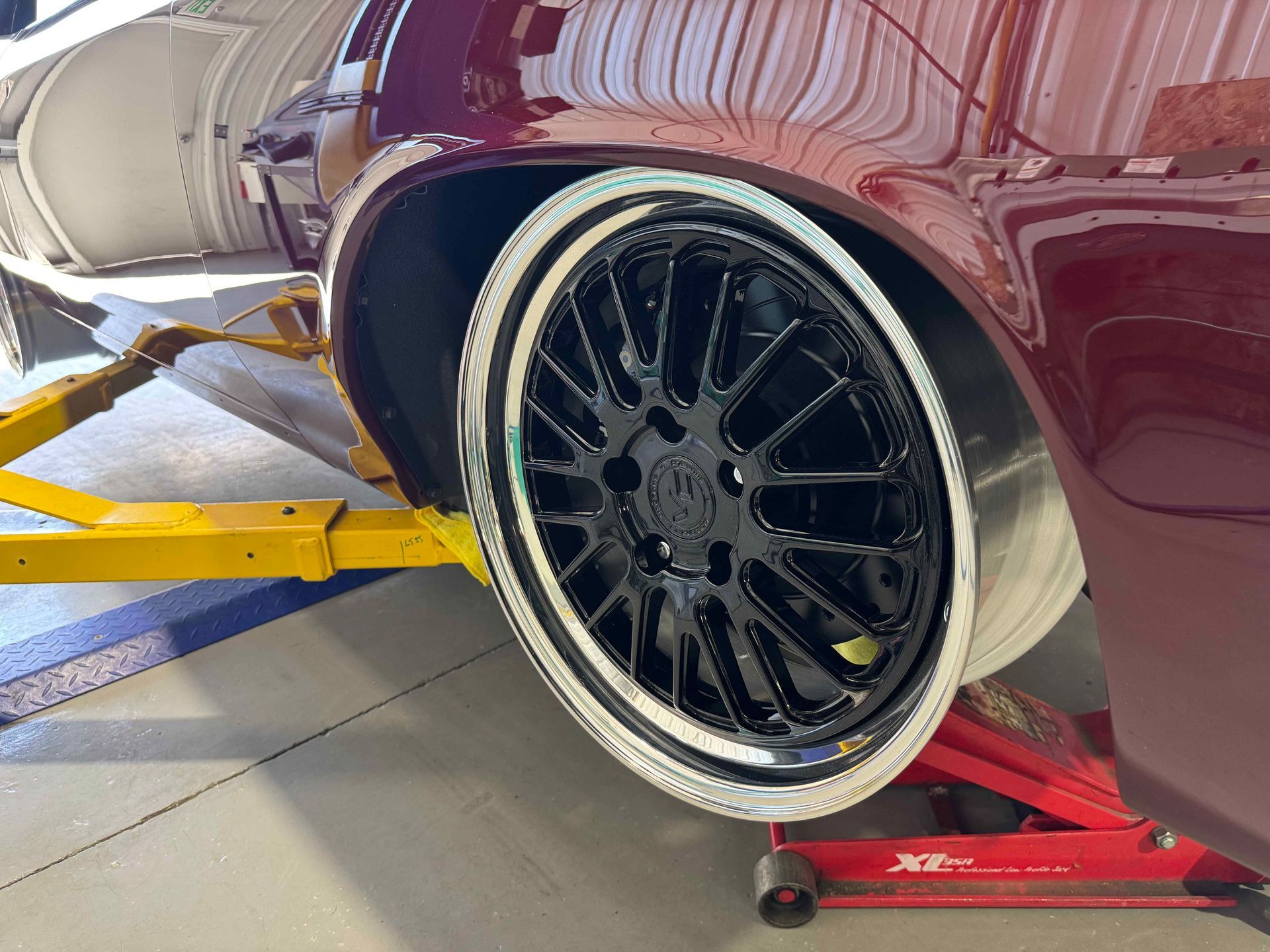 Maroon car on a lift, showing a black alloy wheel and exposed suspension in a garage