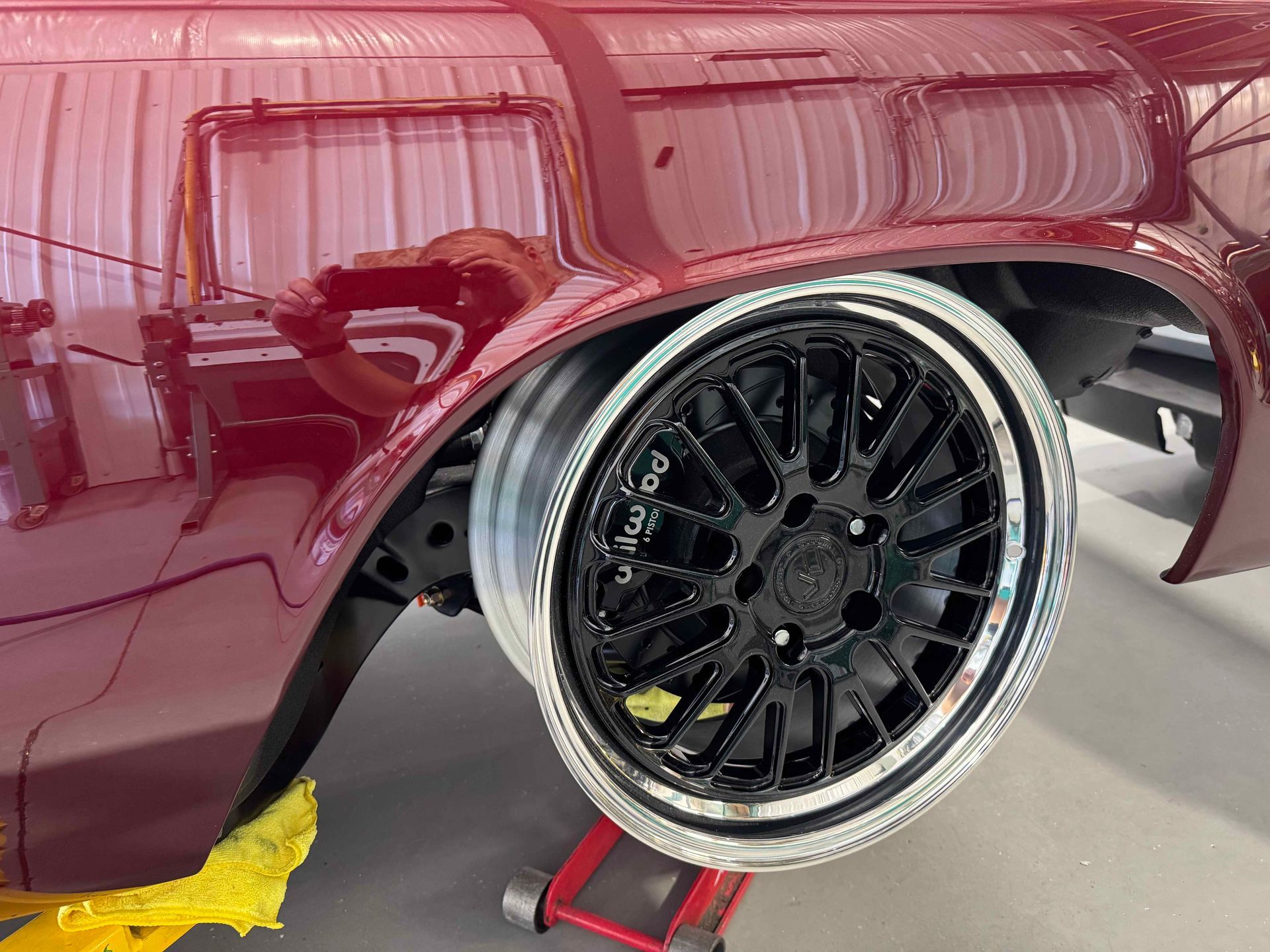 Maroon car body with a custom black mesh wheel on a red stand in a garage