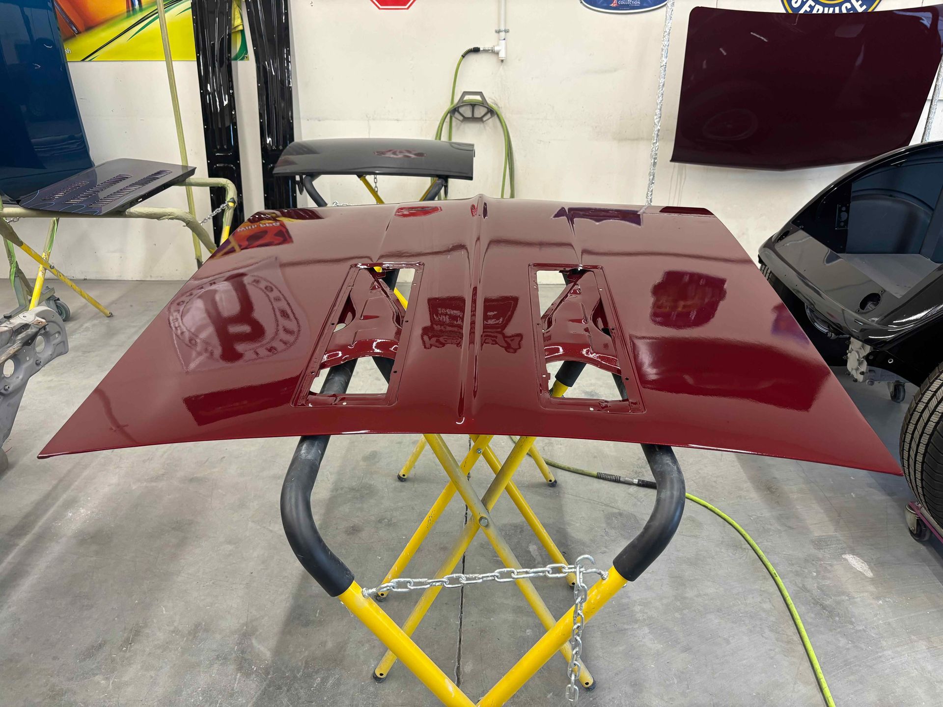 Maroon car hood panel on a stand in an auto body shop with lights reflected on the glossy finish