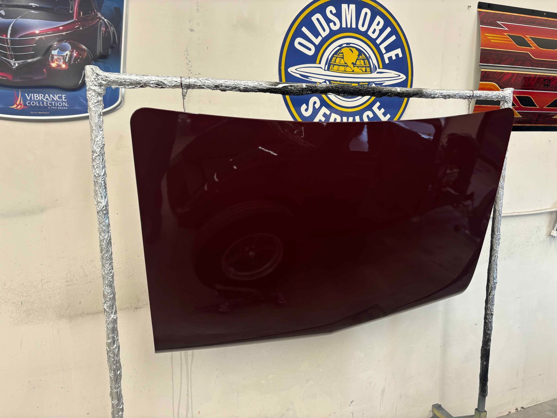 Oldsmobile sign above a dark maroon car hood displayed on a wall