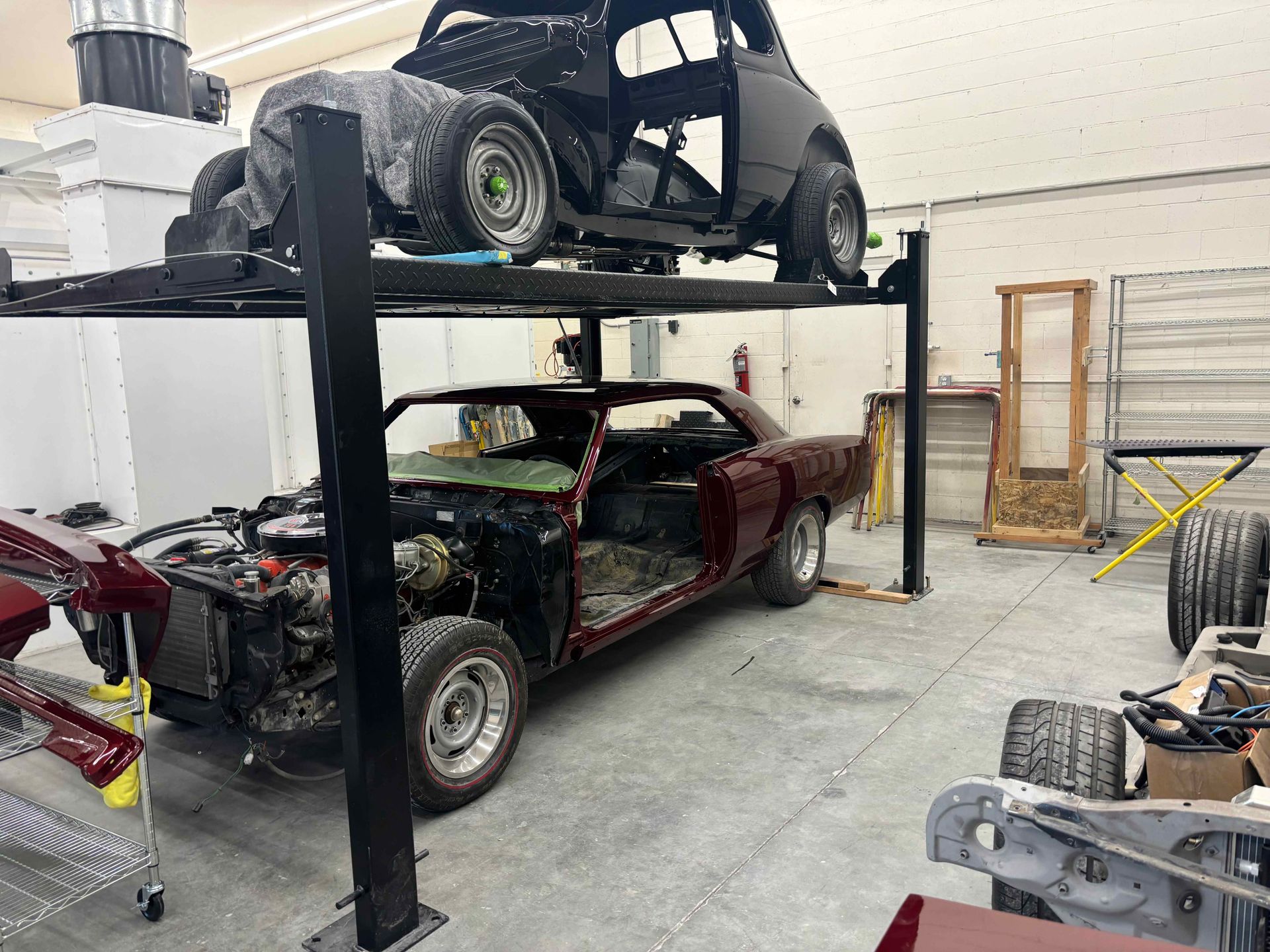 Auto repair shop with two damaged cars on lifts, tools and parts scattered around.
