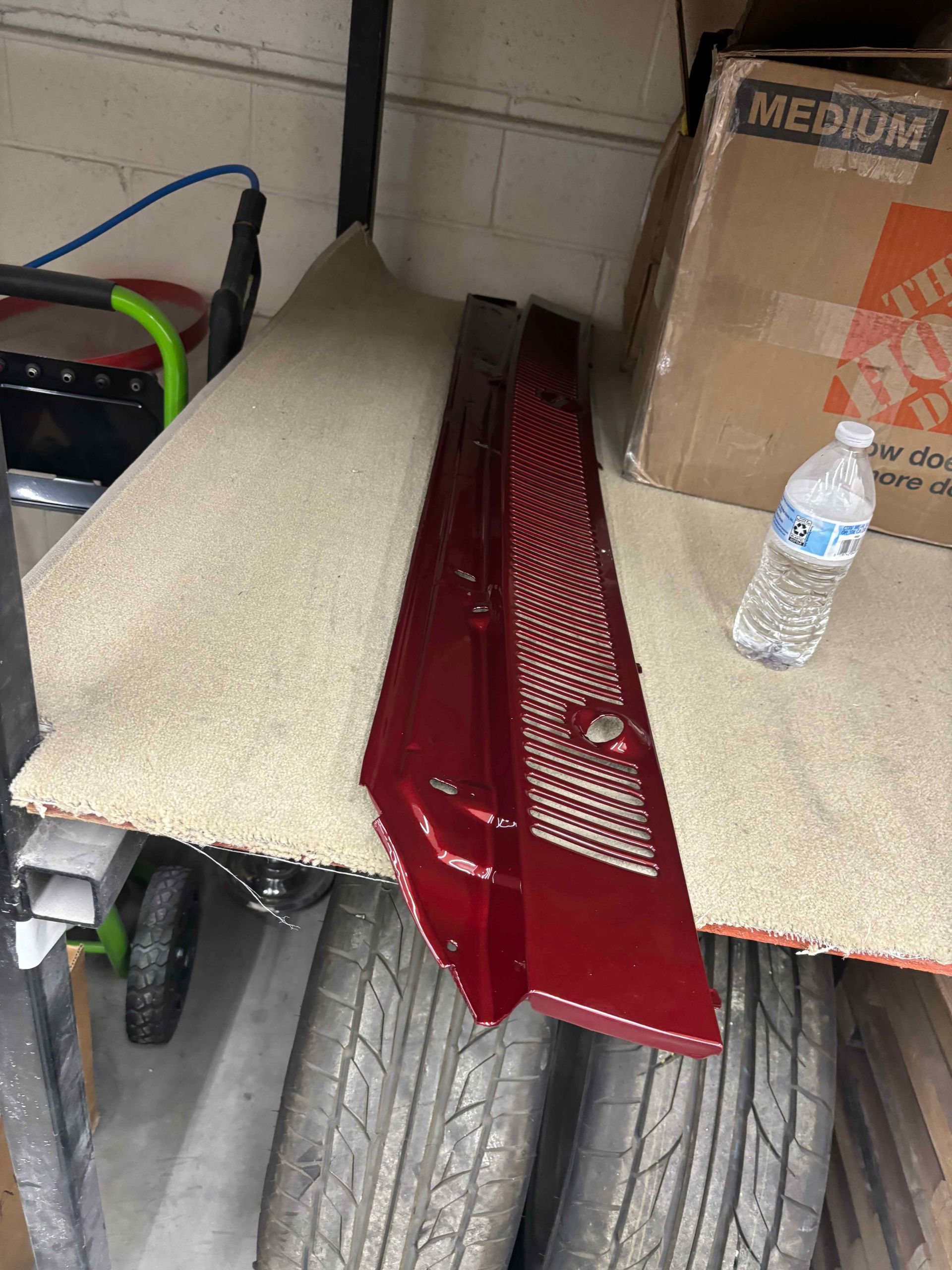 Red car trim and a beige panel leaning against tires in a garage, with a water bottle nearby