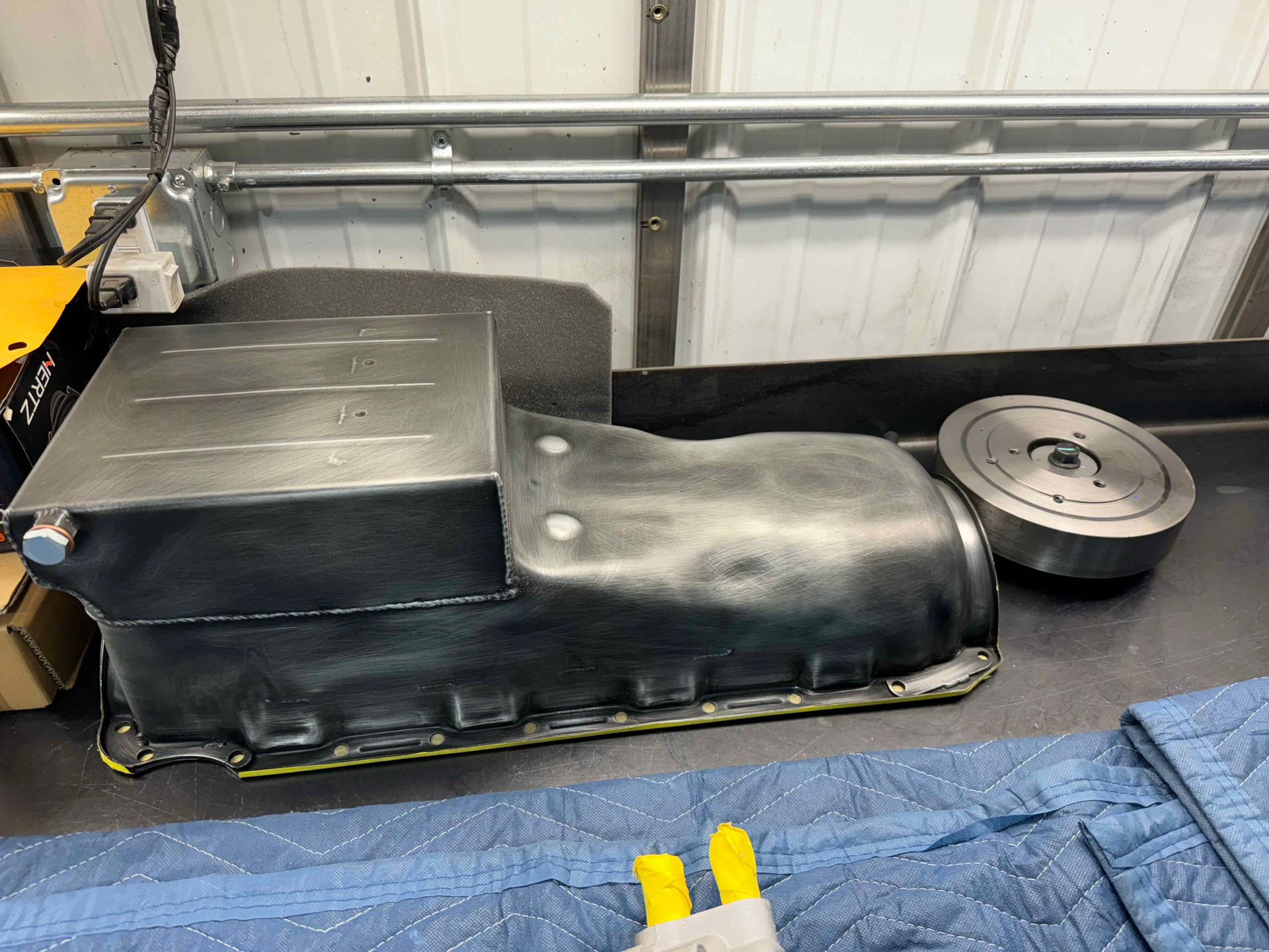Black molded seat or cover on a workbench in a garage, with a round metal part beside it.