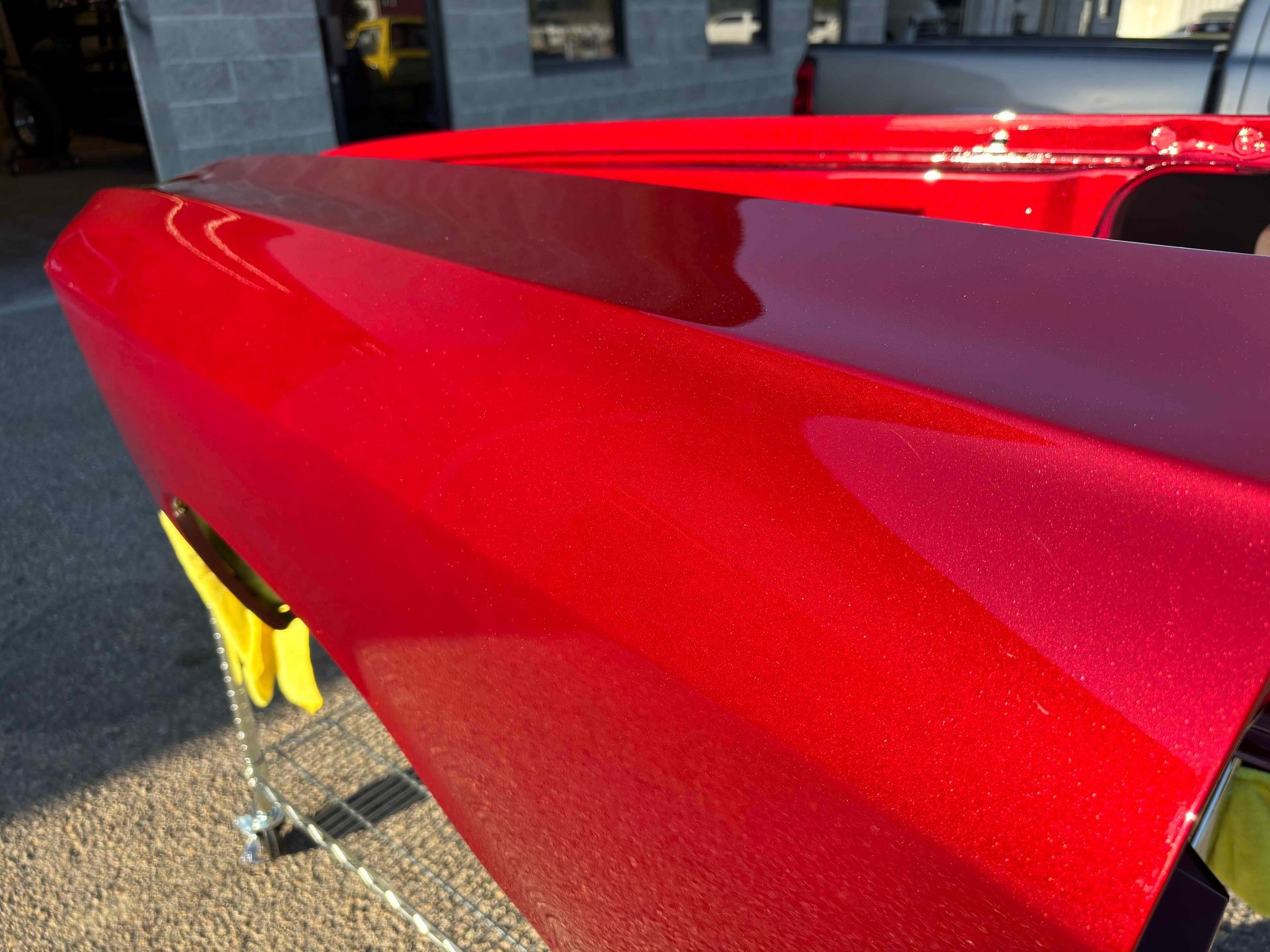 Close-up of a glossy red sports car rear spoiler in sunlight