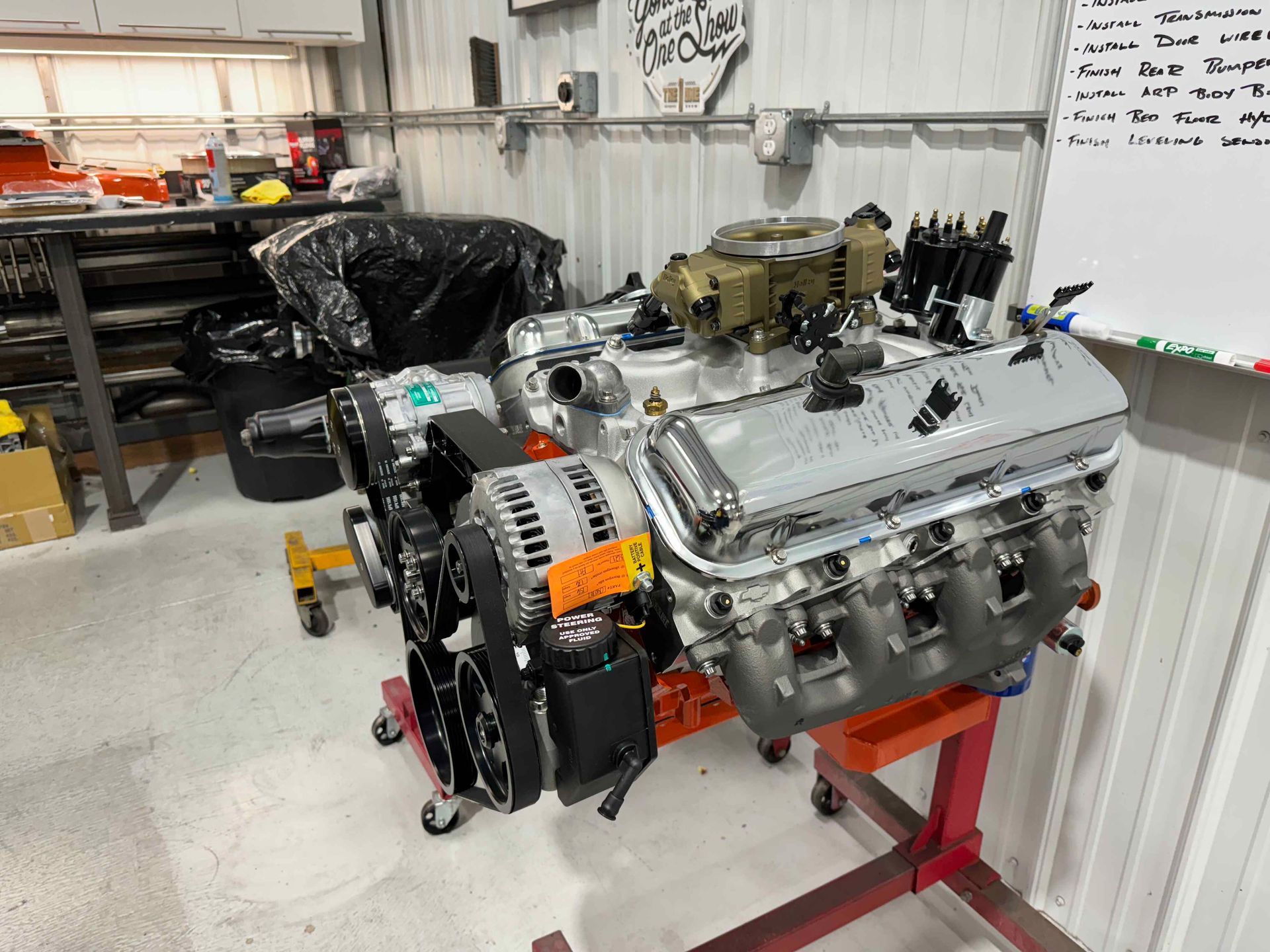 Large engine block on a stand in a workshop, with shelves and tools in the background.