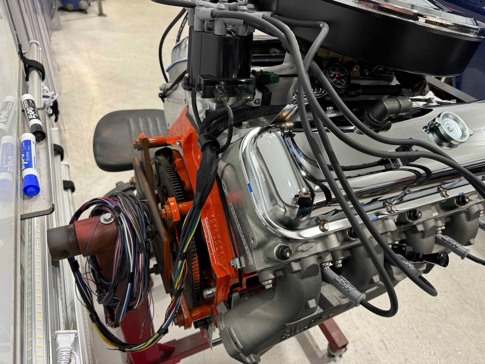Car engine on a stand in a workshop, with hoses and an orange mounting frame.