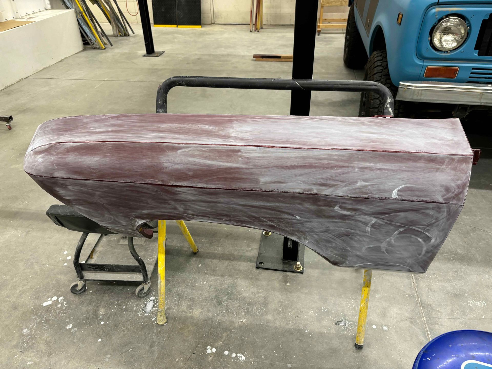 Large maroon foam body panel on a metal stand in a workshop, with a blue vehicle in the background