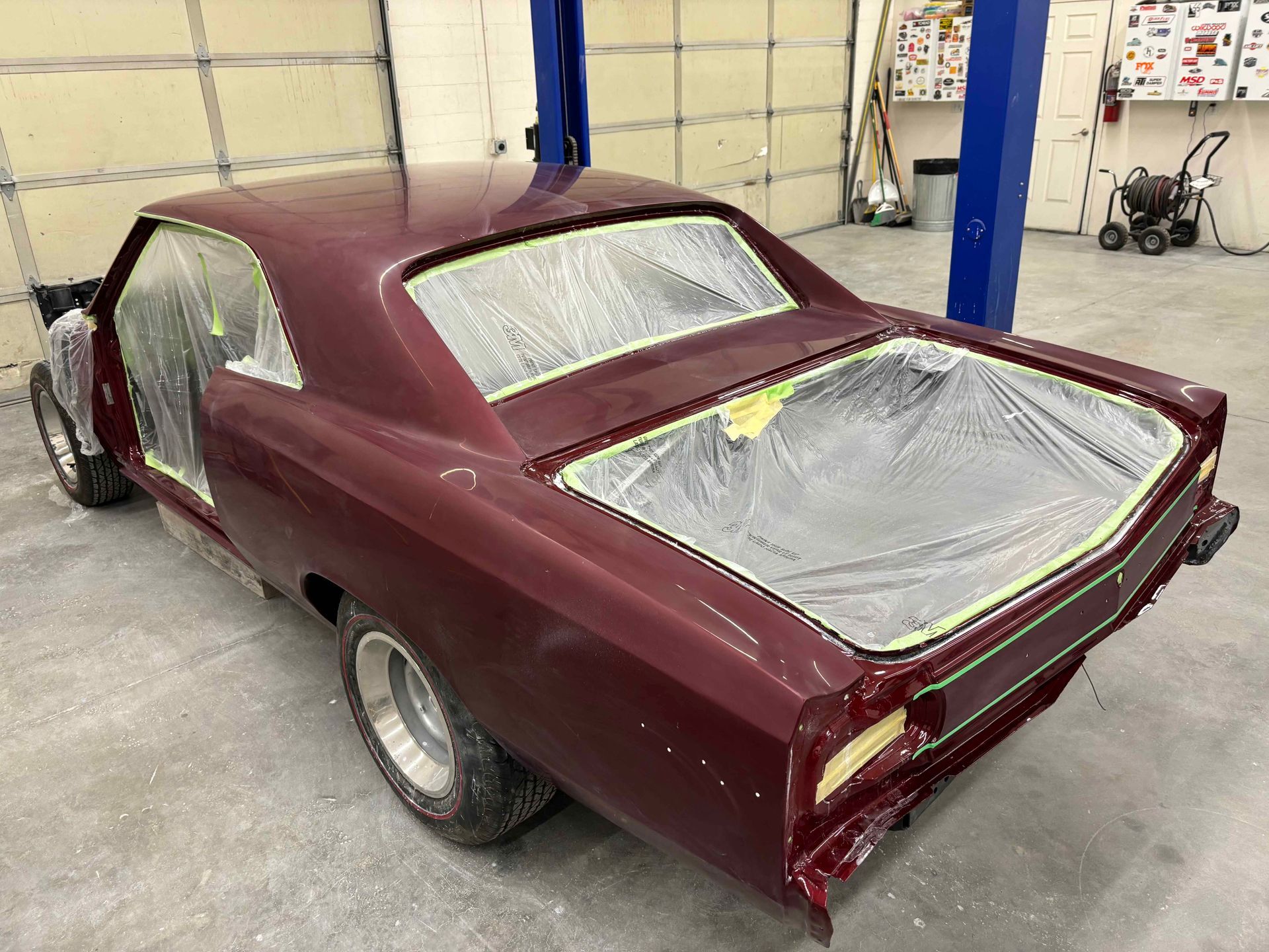 Maroon classic car body in a workshop, masked with protective plastic and ready for paint.