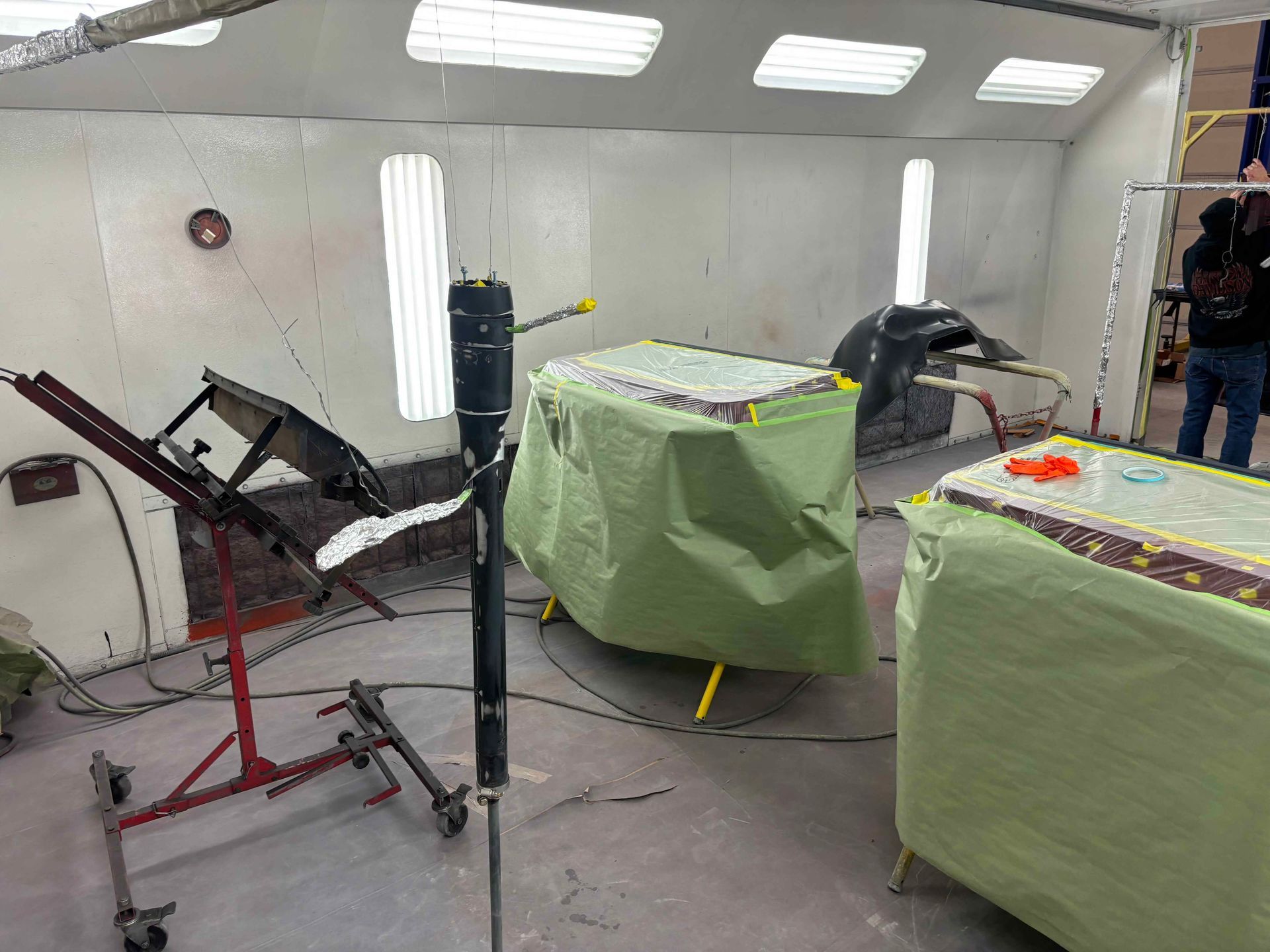 Auto body repair booth with covered car parts, sanding tools, and red-and-white paint booth walls