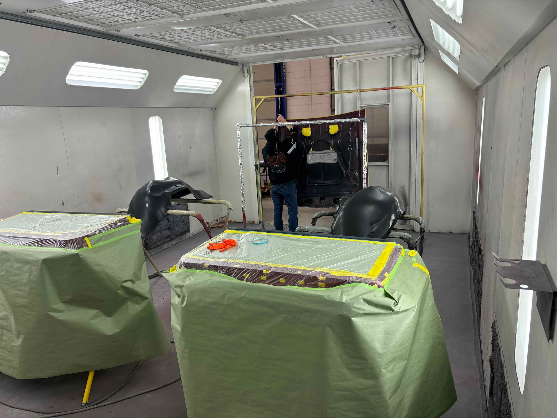 Two green-covered tables inside a small workshop or trailer, with a person near the open doorway.