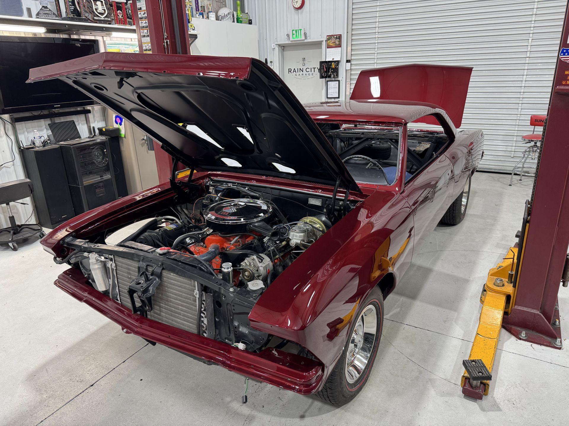 Maroon classic car in a garage with hood open, showing the engine bay on a lift.
