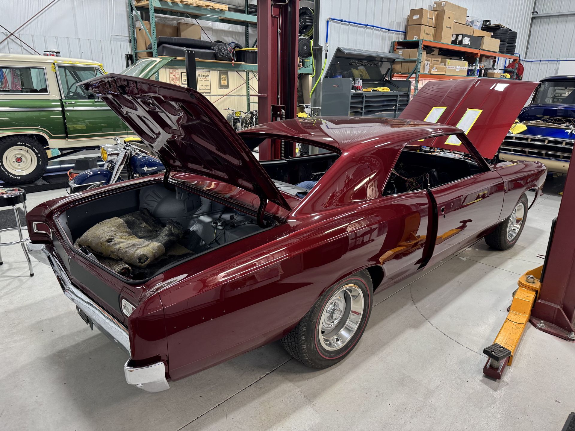 Maroon classic muscle car in a workshop, hood and trunk open for repair