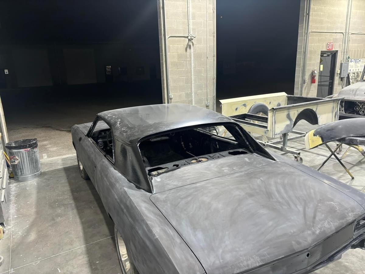 Dust-covered black car body inside an industrial workshop with open bays and equipment nearby