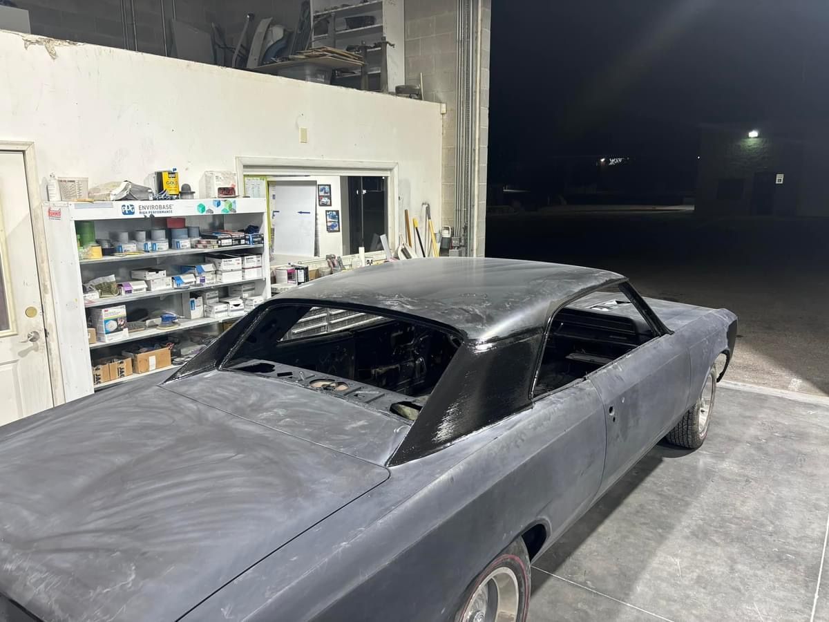 Matte black classic car body in a garage, with shelves and an open doorway in the background