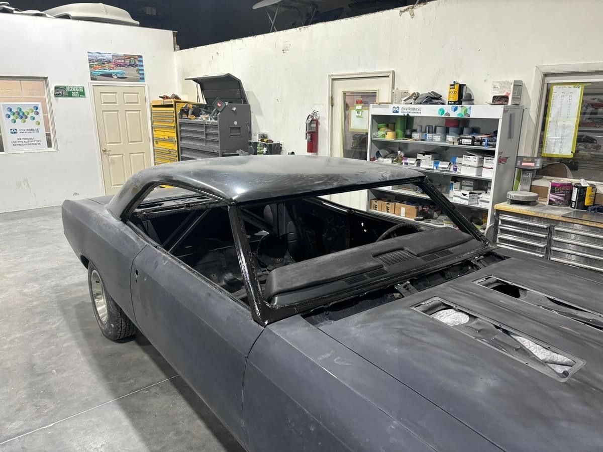 Gray car body in a garage workshop, with a stripped interior and open hood area.