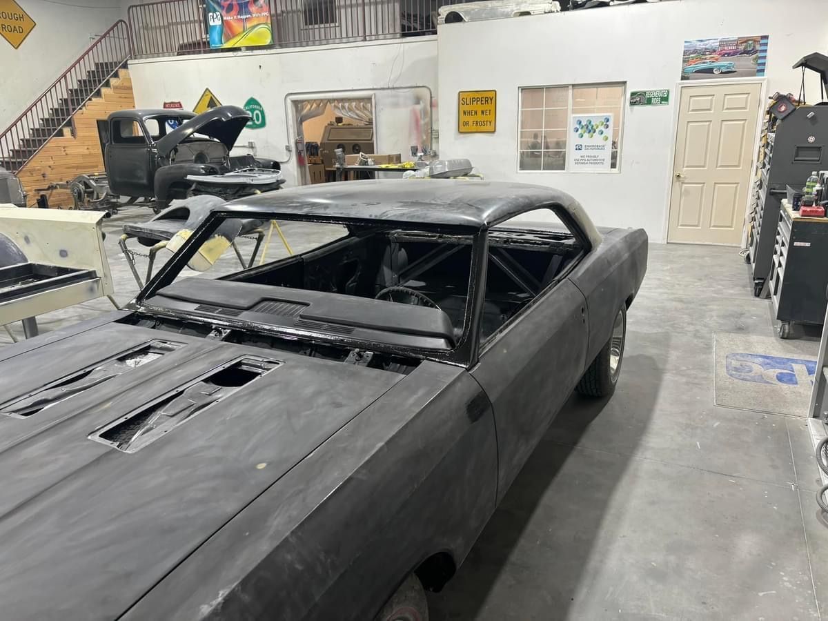 Black classic car in a workshop with a partially removed roof and hood, surrounded by tools and equipment.