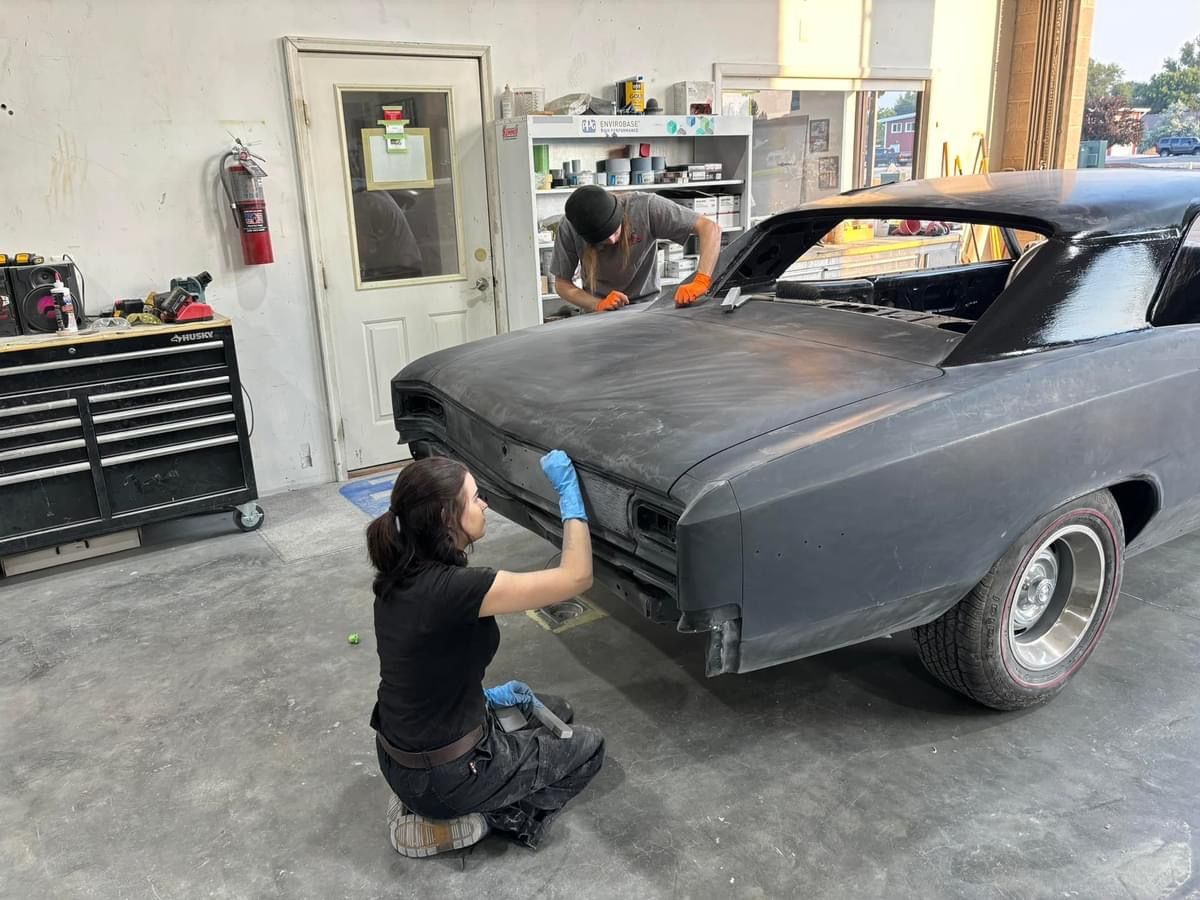Two mechanics sanding a black classic car body in an auto shop