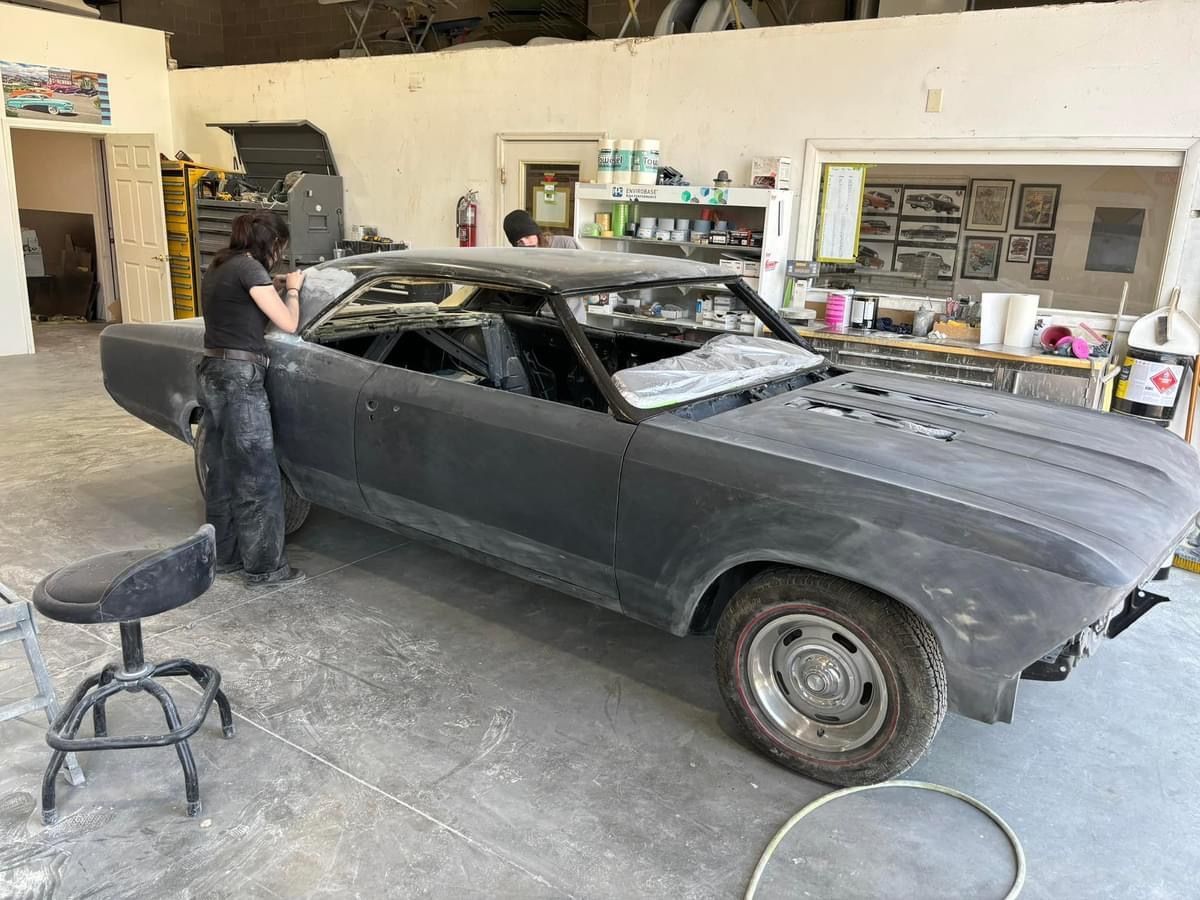 Person sanding a matte black classic car in a garage workshop