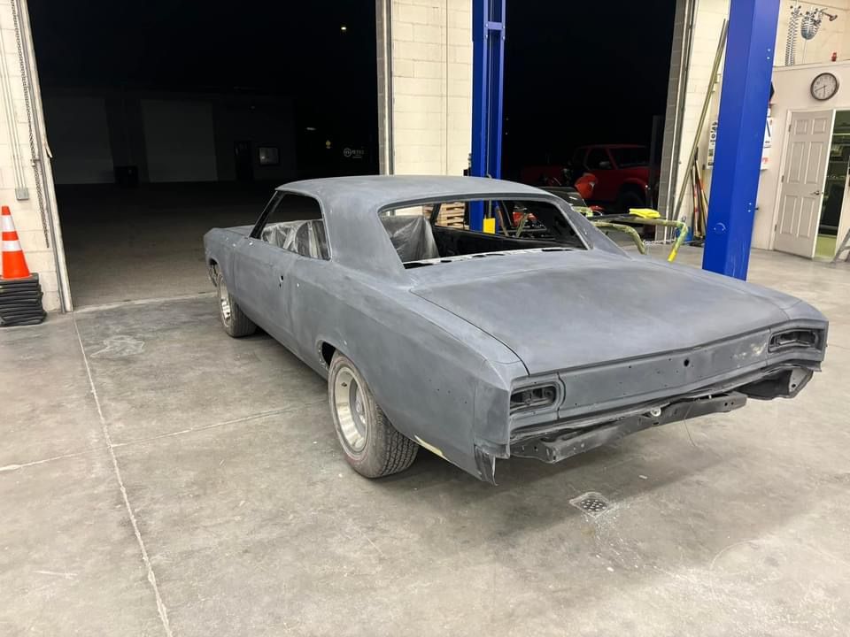 Gray classic car under repair in a garage, with primer coating and missing windows