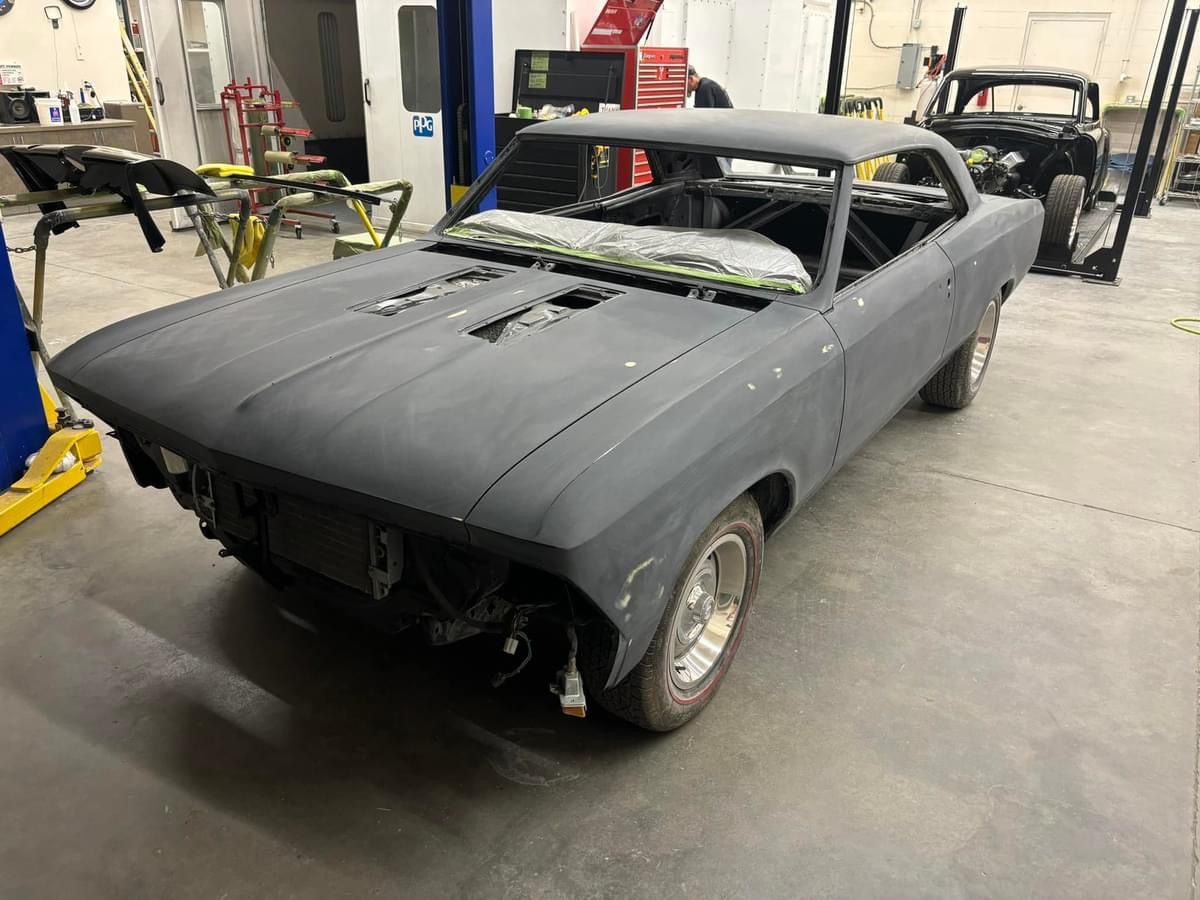 Black classic car shell in a garage, missing front end and windows, under restoration