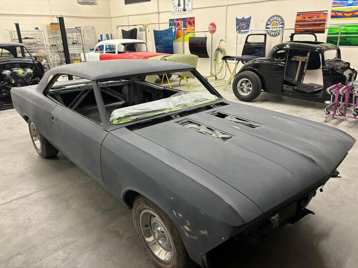 Matte gray classic car shell in a workshop, with missing trim and open front end.