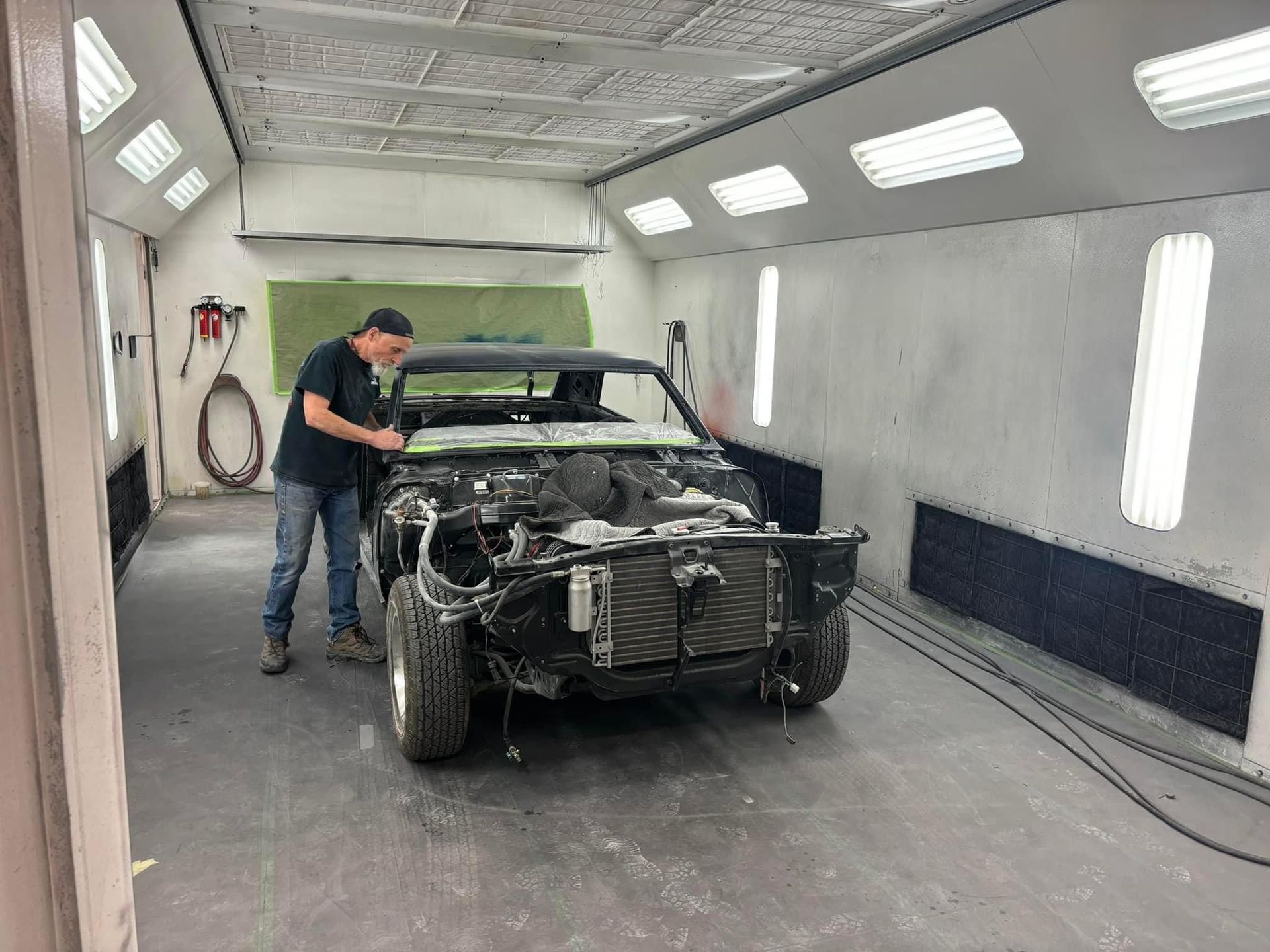 Man spraying a black car body in a paint booth, with the front bumper removed