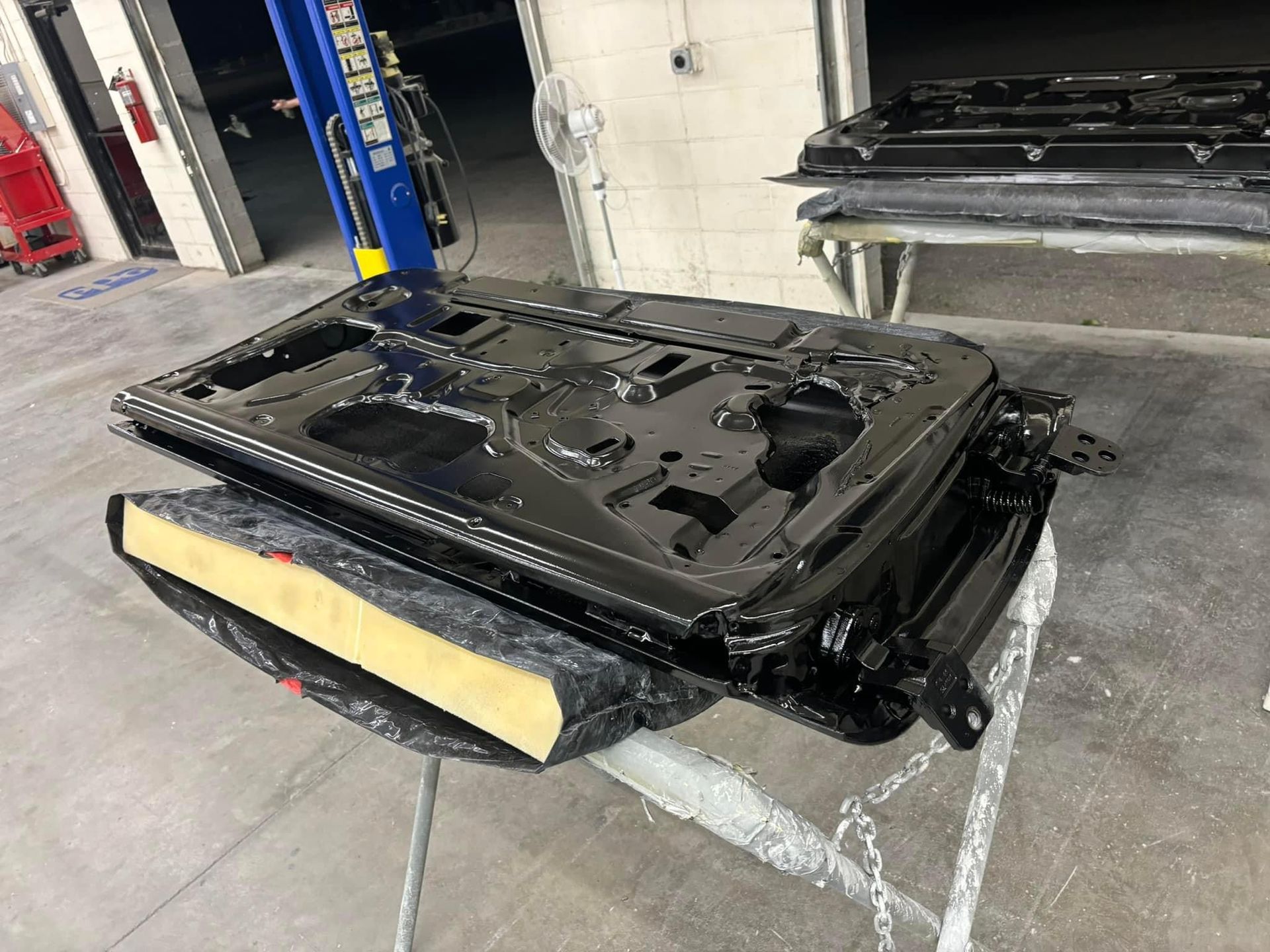 Black car bumper cover on a shop floor beside a lift in an auto repair garage