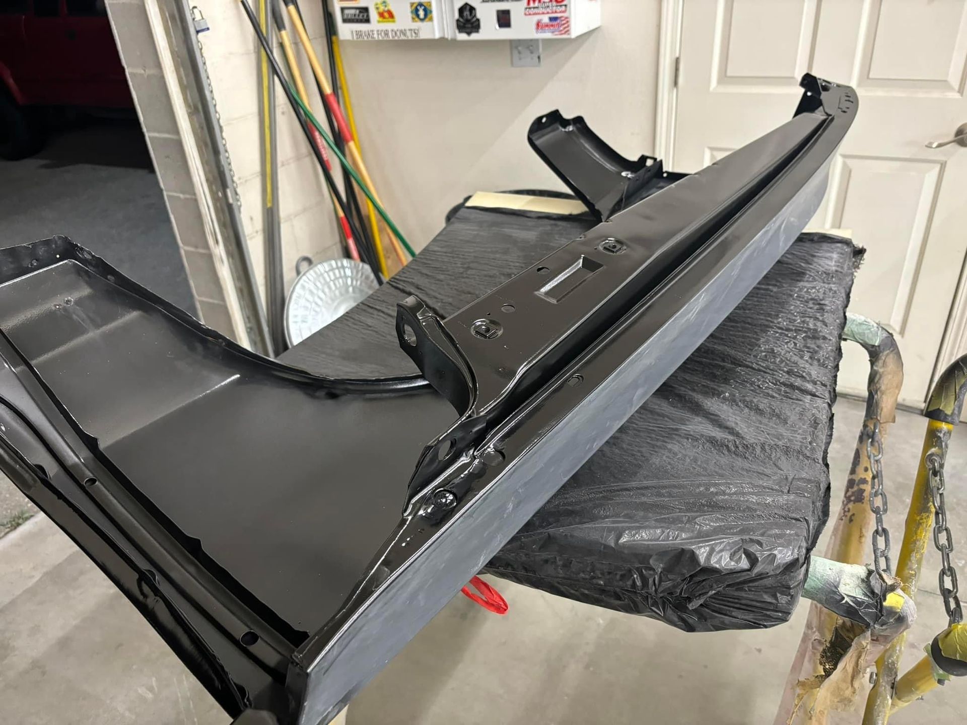 Glossy black car bumper cover propped on a wrapped stand in a garage
