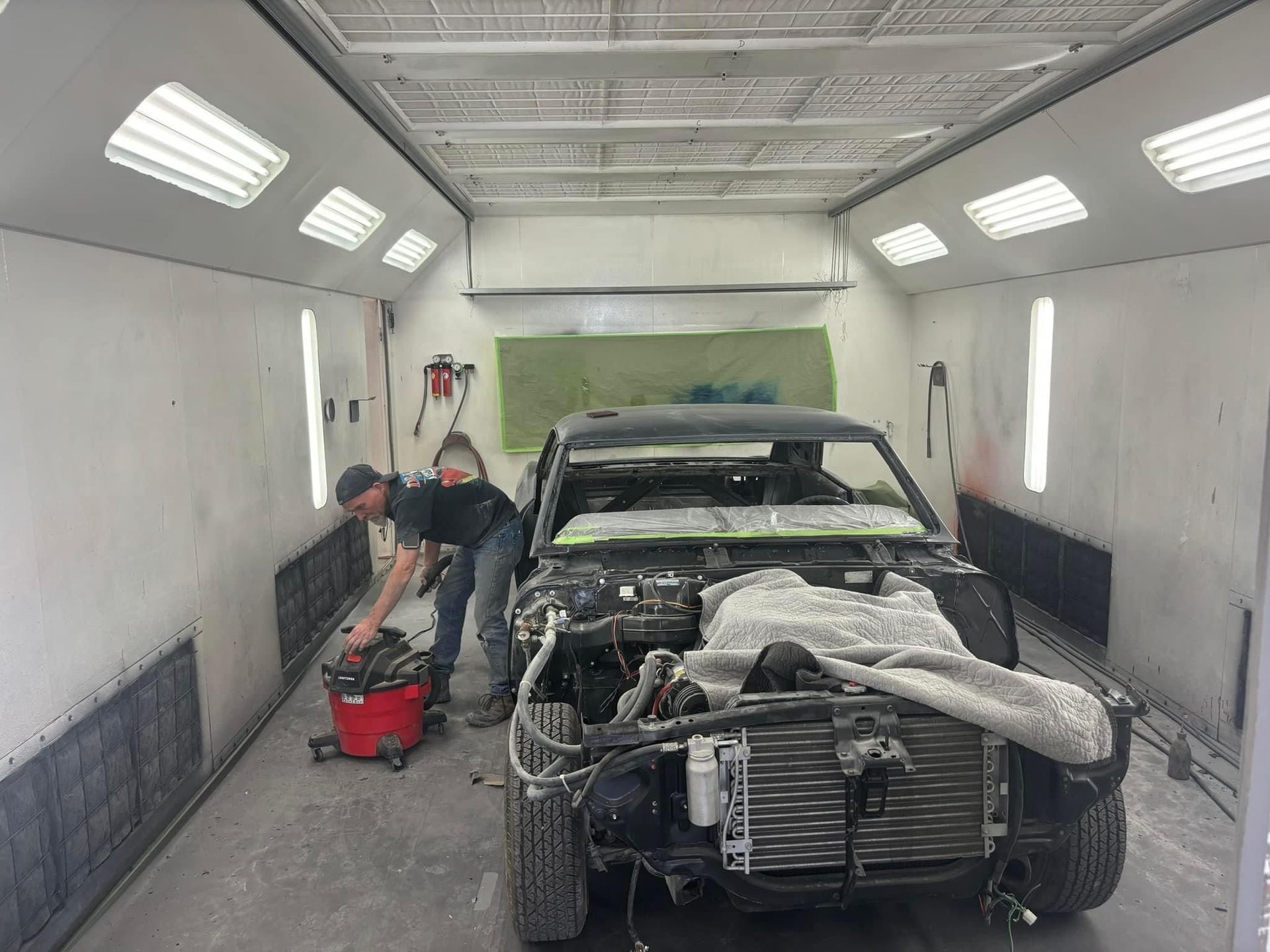 Auto body repair shop with a car under repair and a person working beside it in a paint booth