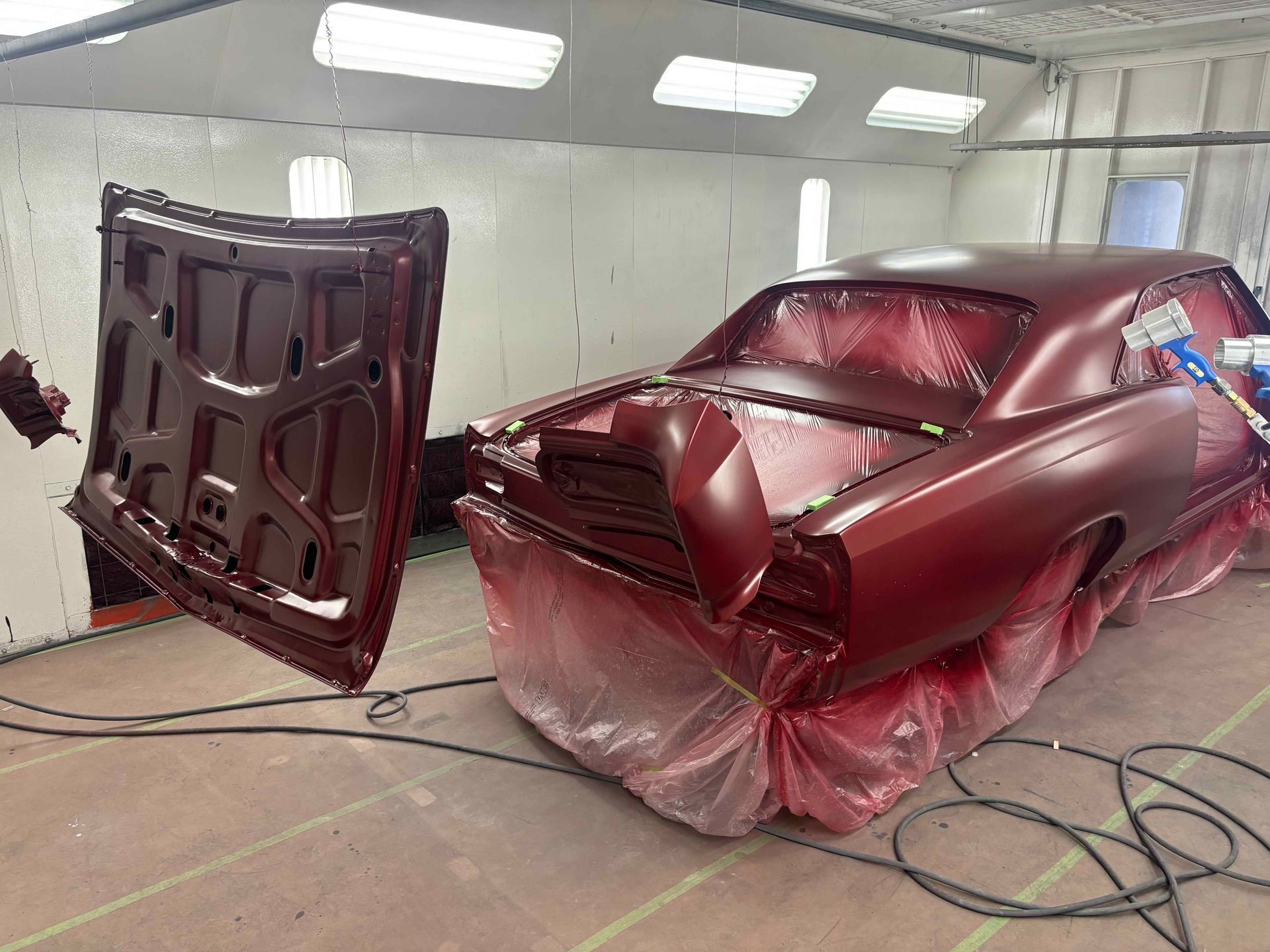 Red car body parts in a spray booth, with doors open and covered in red masking plastic.