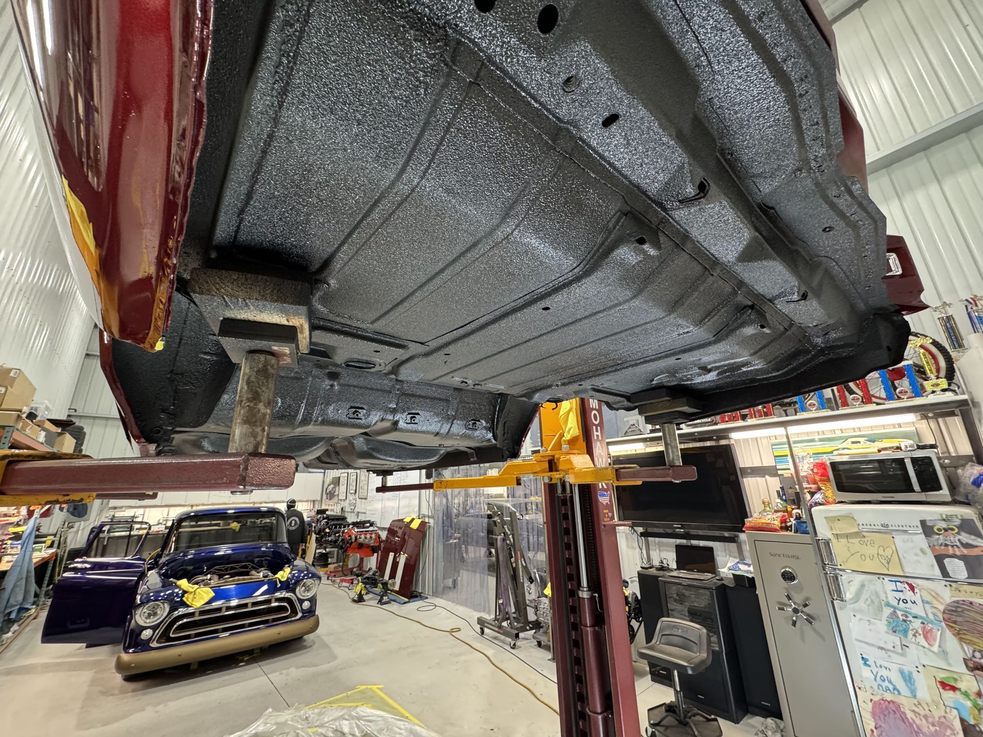Classic car lifted on a garage hoist, showing the underside in a busy auto shop