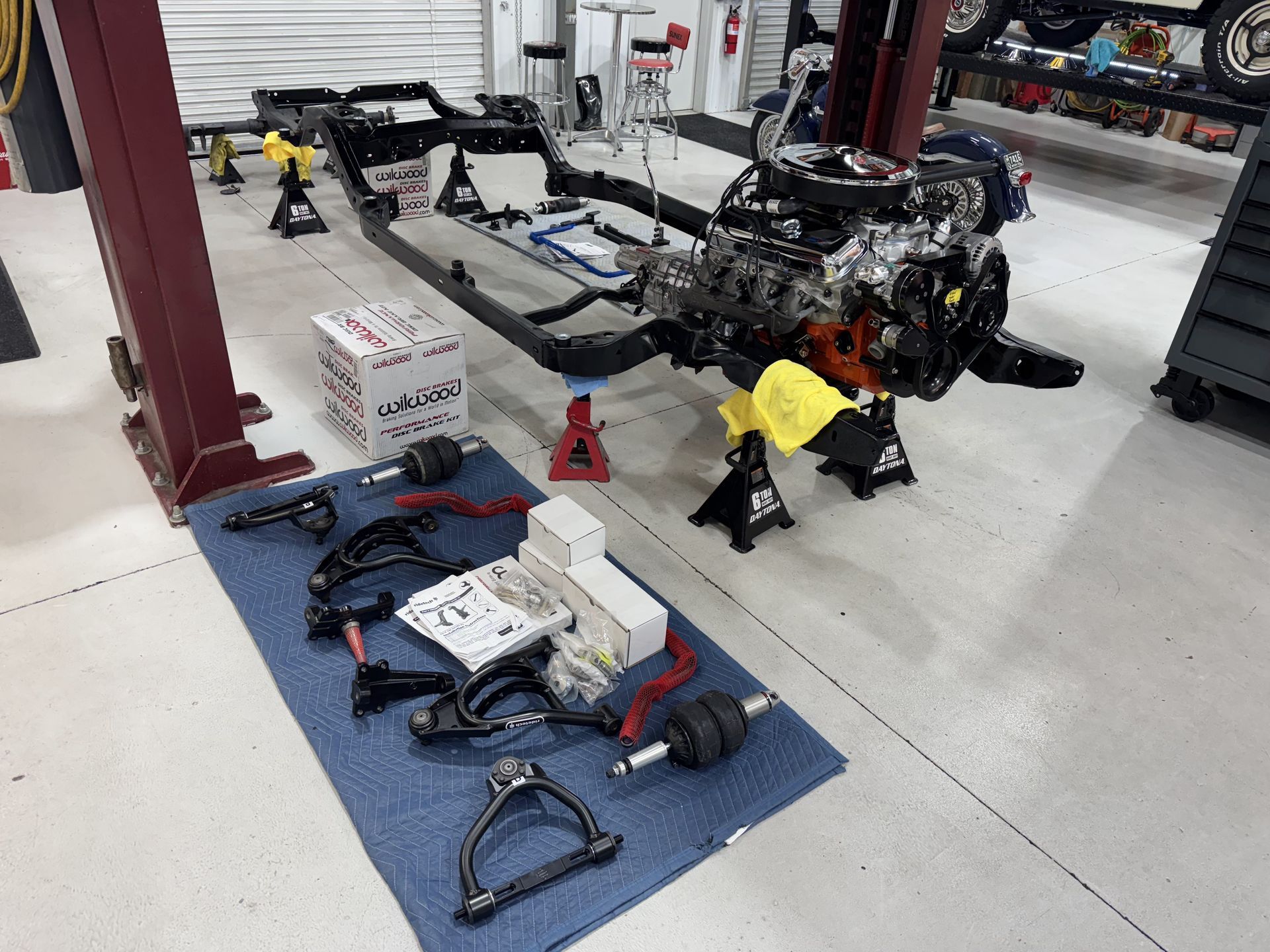 Car chassis in a workshop, with engine parts and tools laid out on the floor and nearby stands.