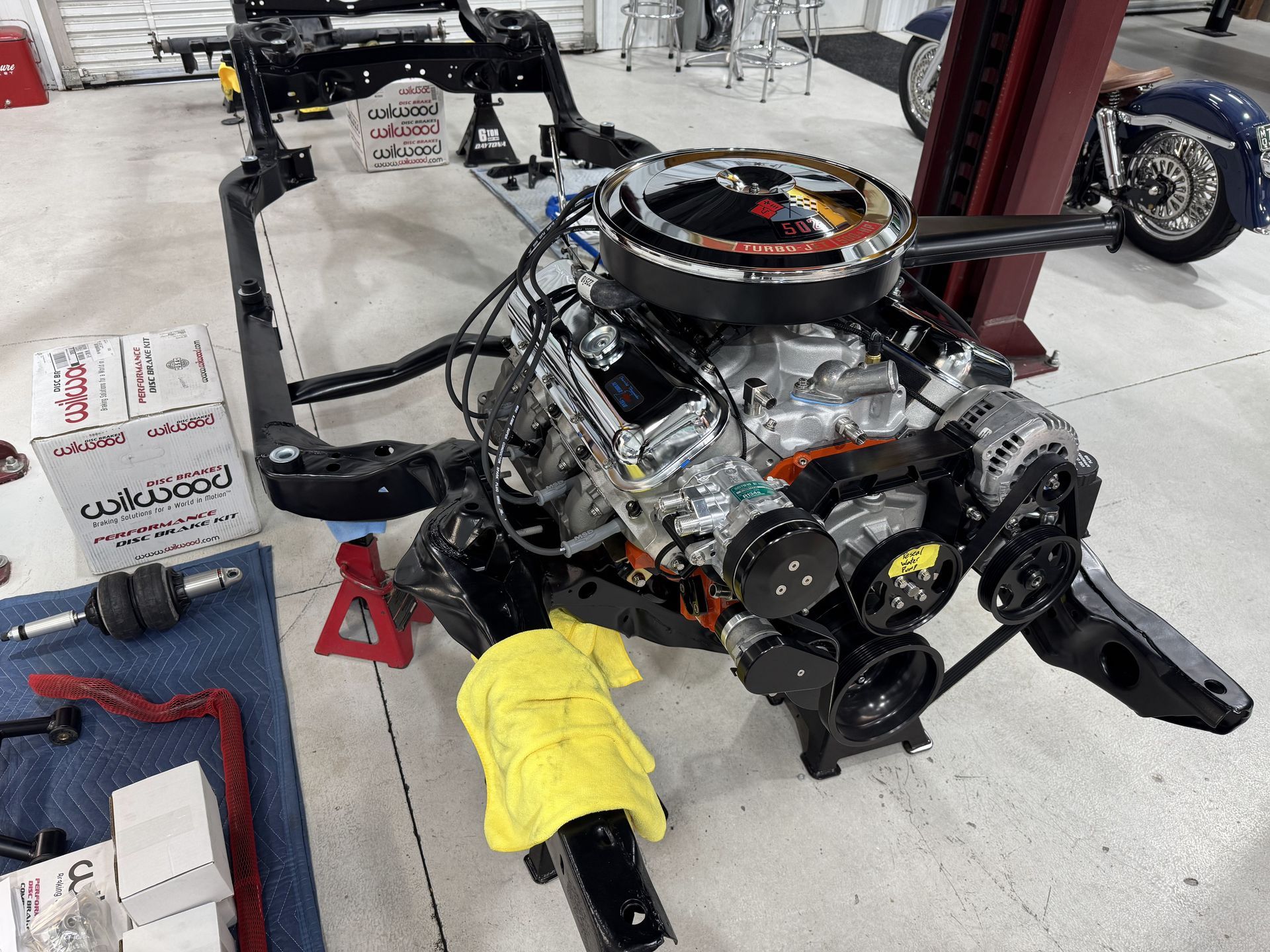 Car engine on a stand in a bright garage, with tools and parts around it