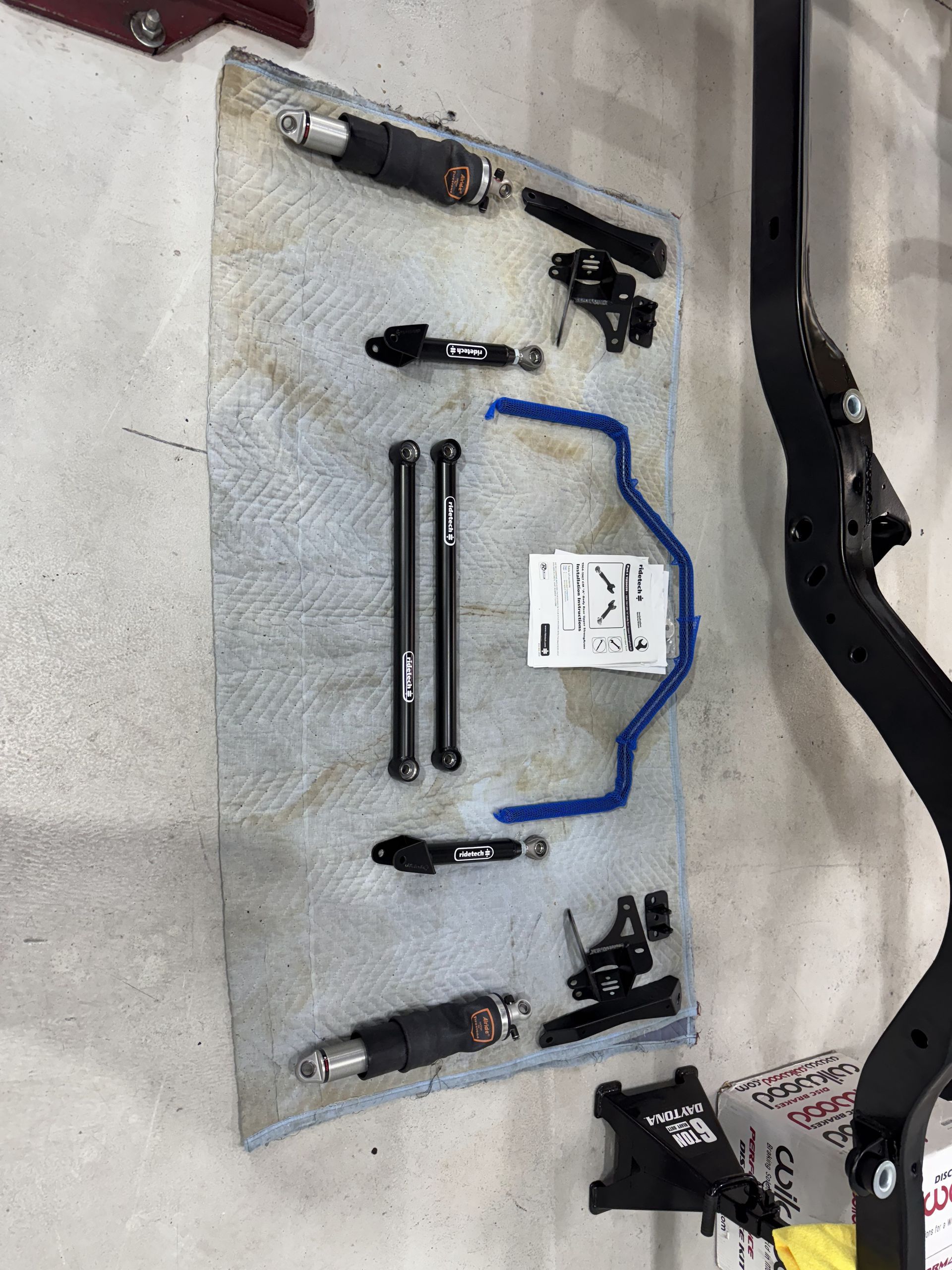 Car parts and tools arranged on a gray mat, with black metal components, bolts, and a blue cable.