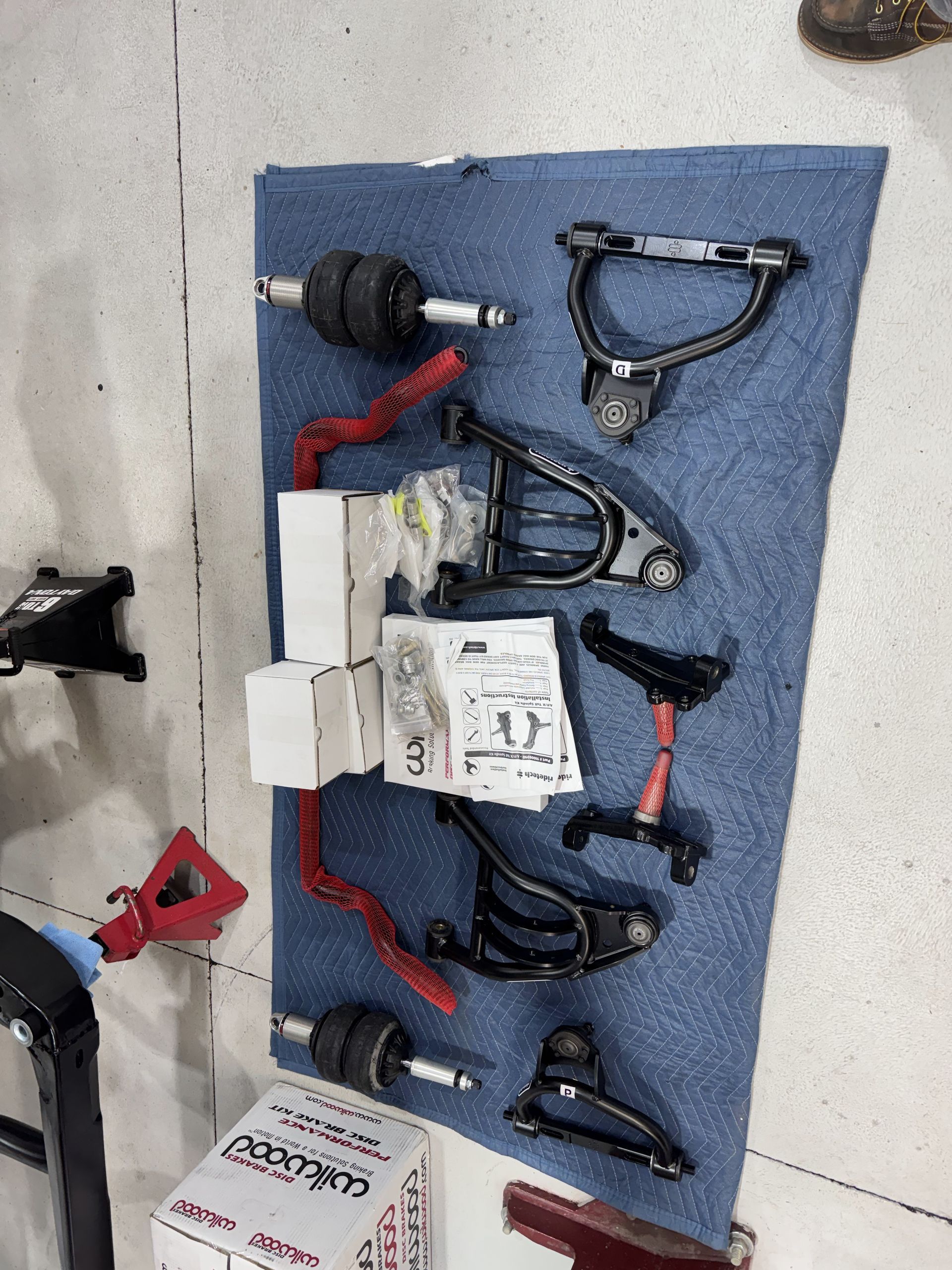 Assorted black and red metal hardware parts arranged on a blue mat on a tiled floor.