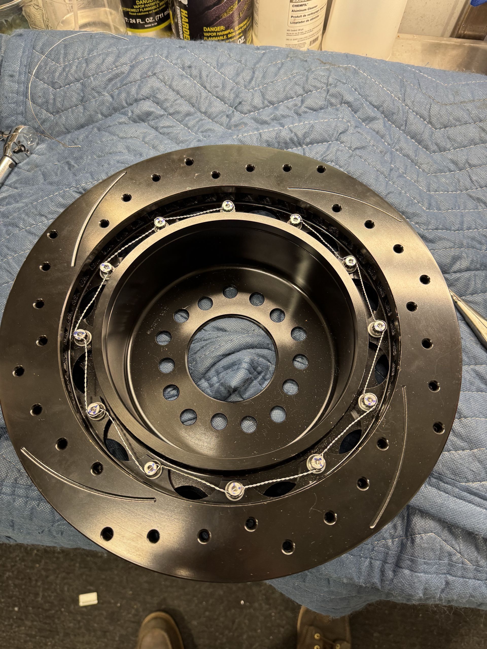 Black perforated metal brake rotor or disc resting on a blue quilted blanket.