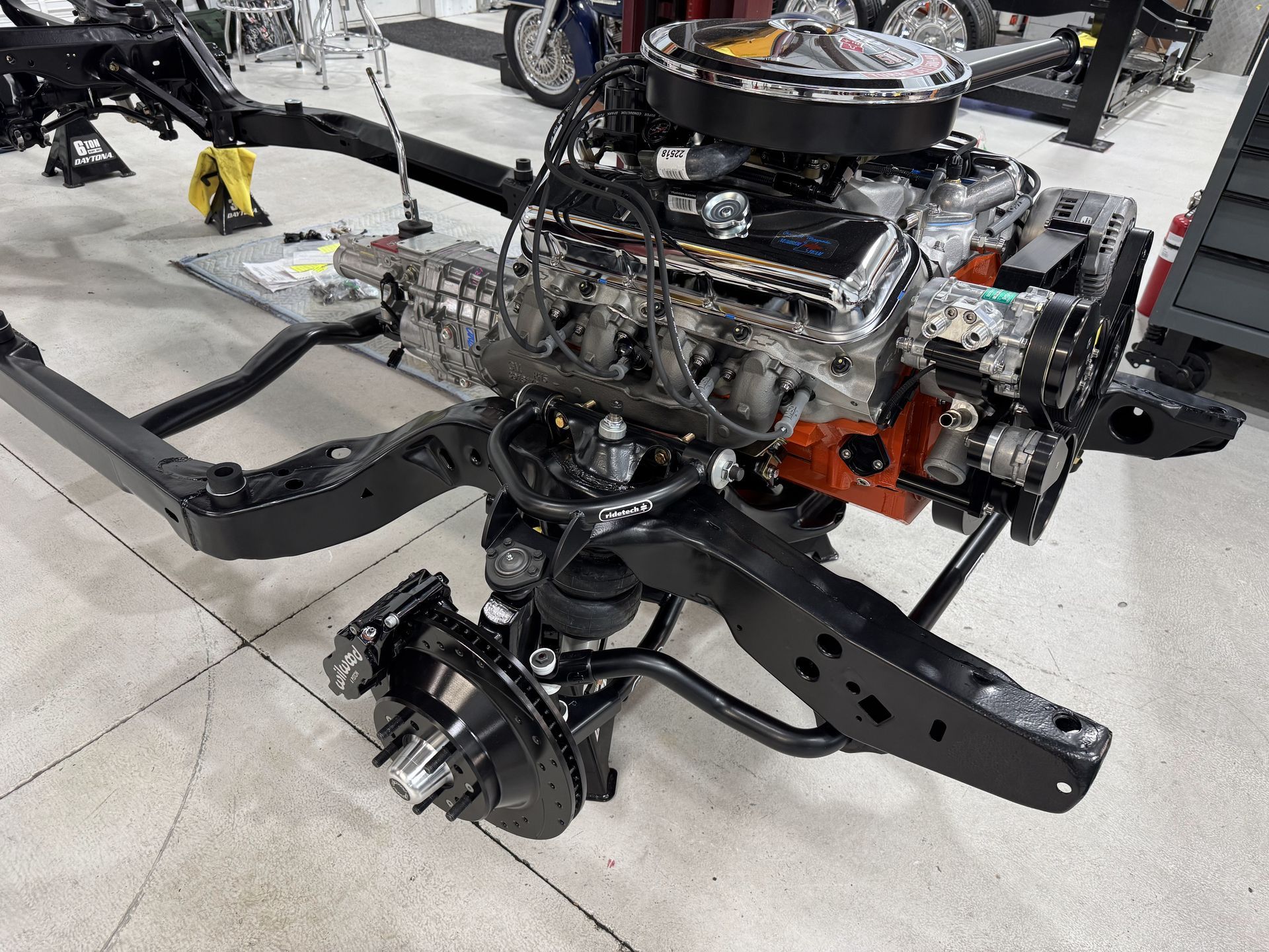 Bare car chassis with exposed engine and suspension in a workshop.