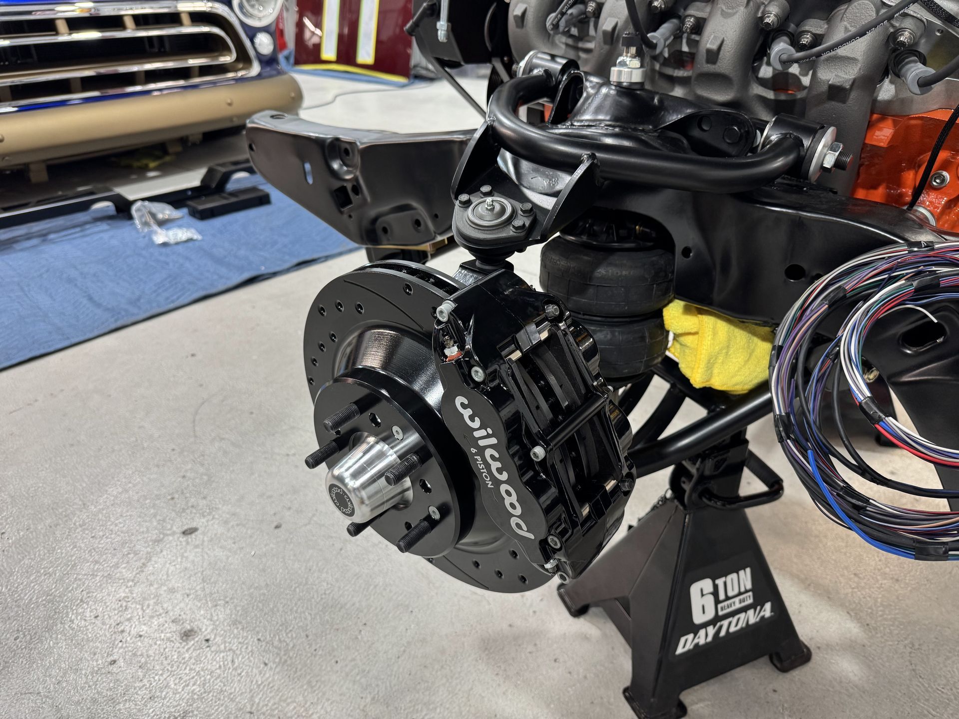 Brake and suspension assembly on a car in a garage, with exposed front wheel hub and coiled hoses nearby