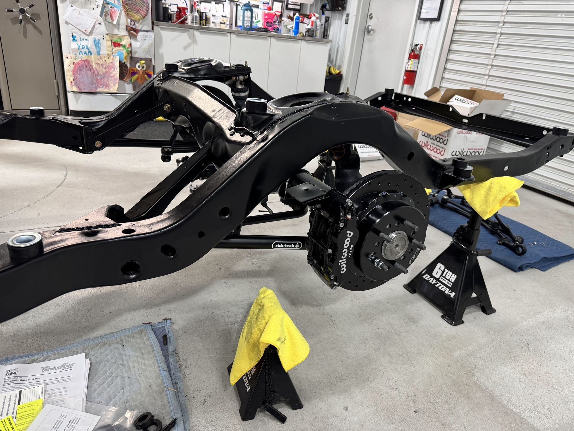 Black vehicle chassis on a workshop floor with exposed rear axle and tools nearby