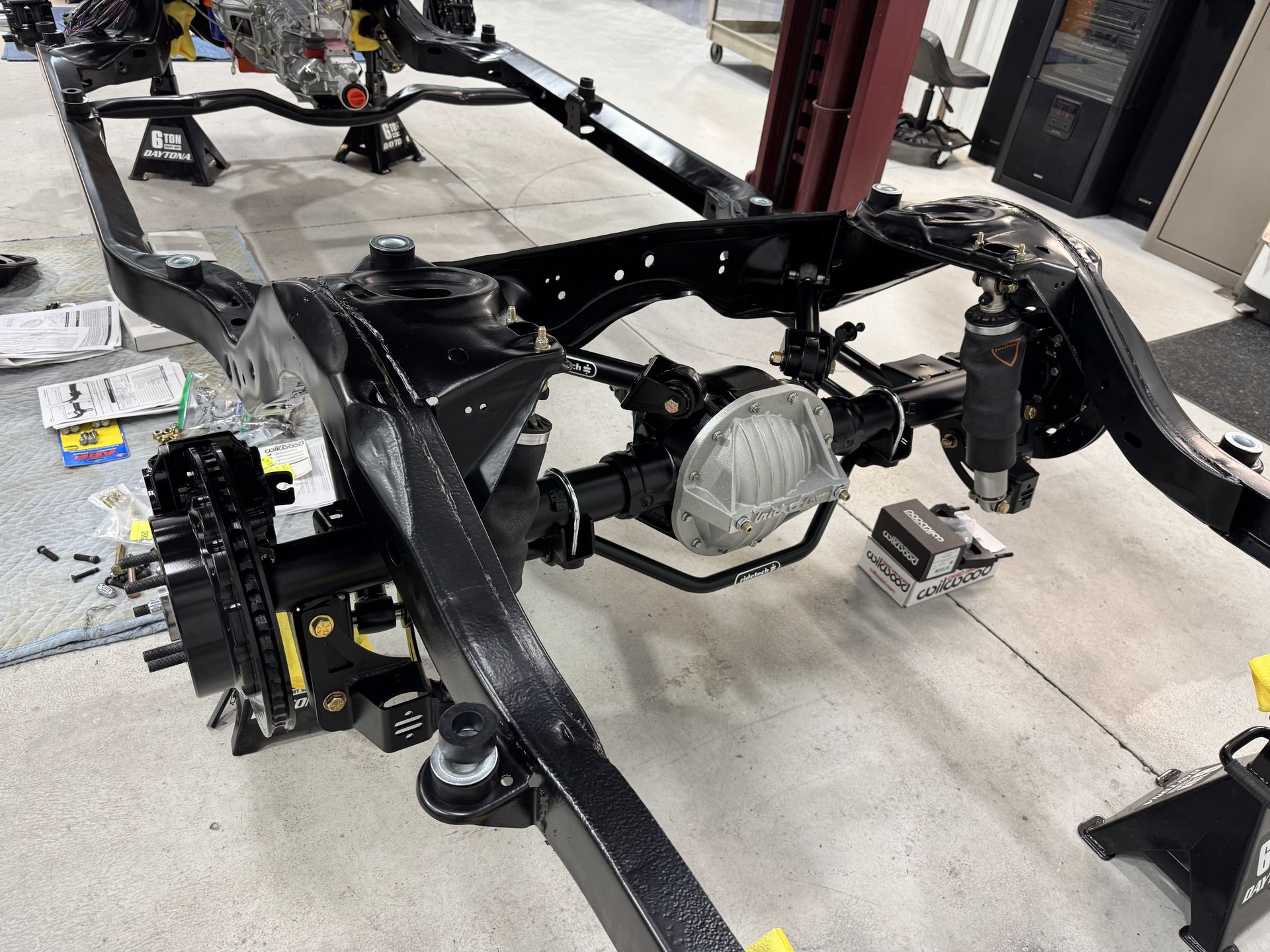 Bare vehicle frame chassis in a workshop, with suspension parts and tools on the floor