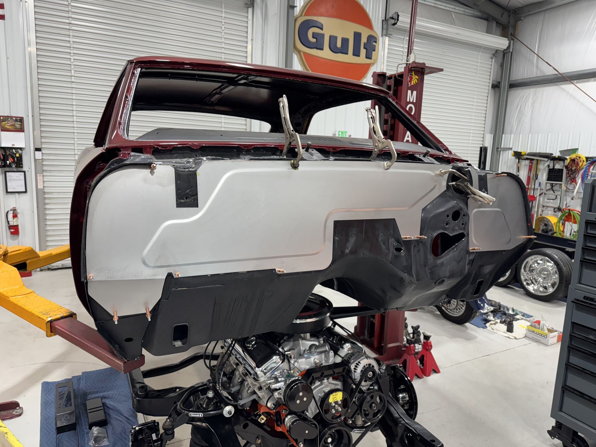 Partially stripped red car body in a garage with its engine exposed underneath.