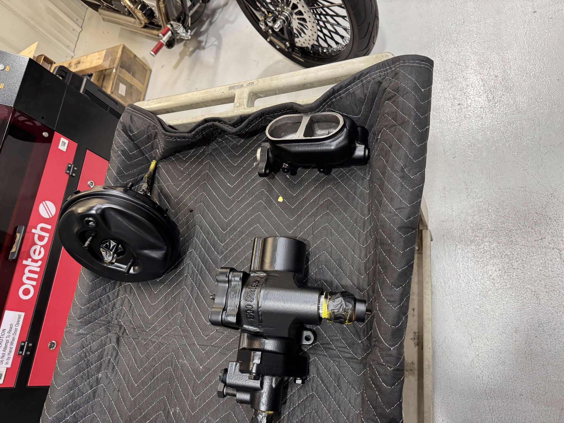 Car steering components and wheels laid out on a padded mat in a workshop