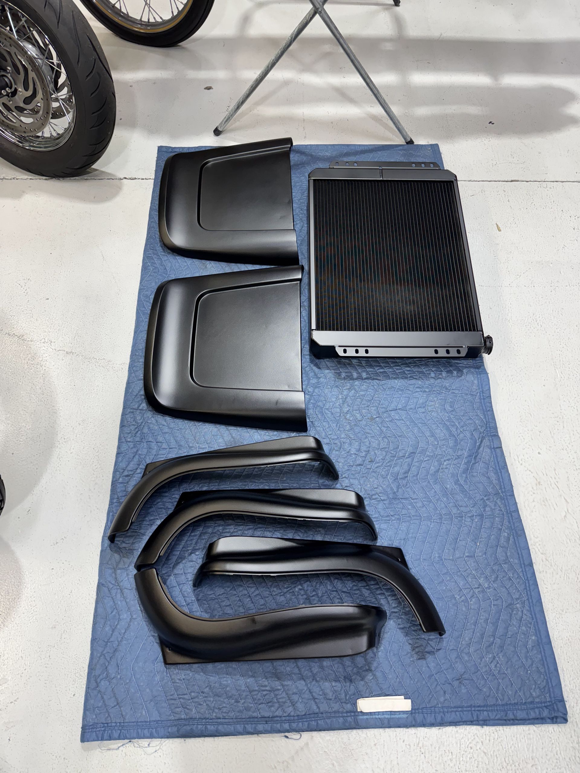 Assorted black plastic motorcycle fairing parts laid out on a blue mat in a garage.