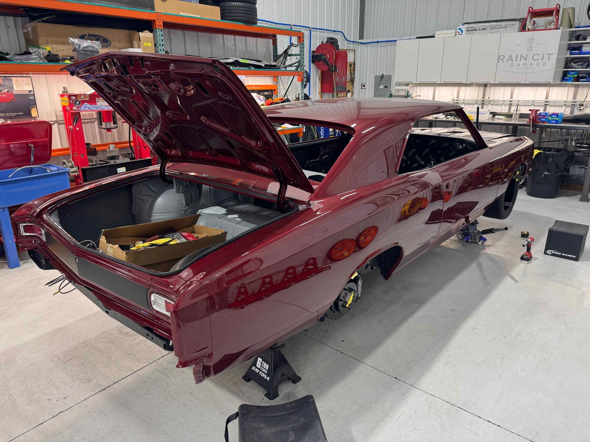 Maroon classic car in a workshop, rear hatch open, with tools and equipment around it