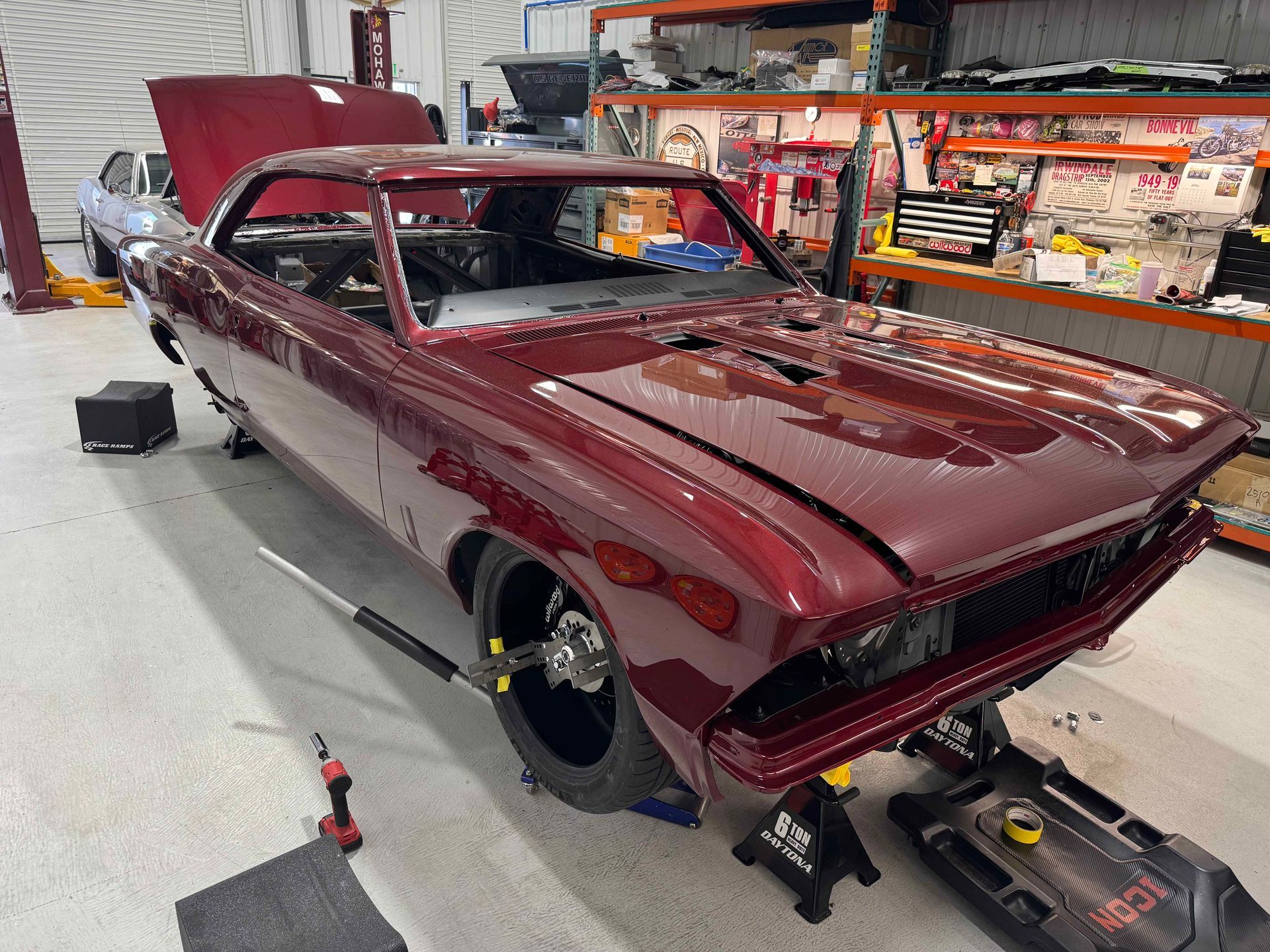 Maroon classic car in a workshop, undergoing restoration with wheels off and tools nearby
