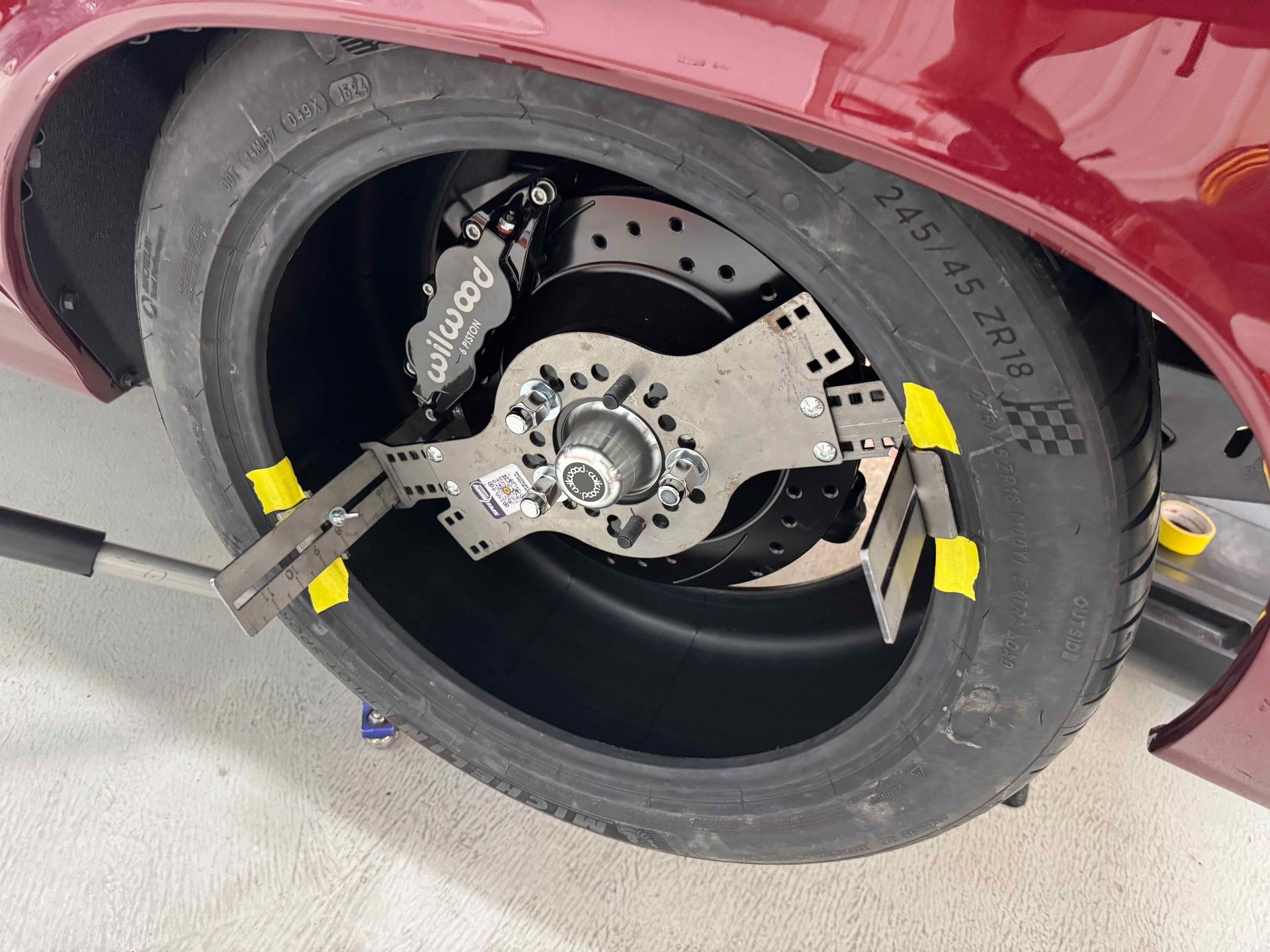 Car wheel lifted off the ground, showing brake rotor and suspension components with yellow clamps.